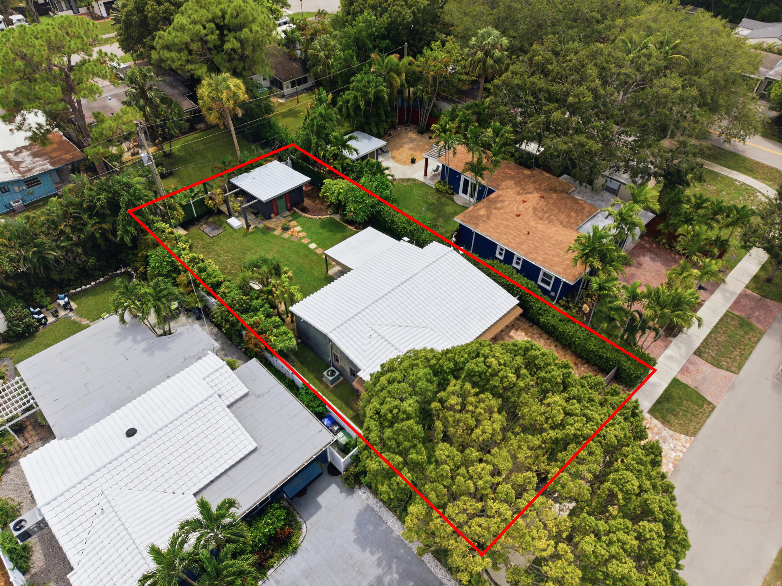 Aerial perspective of a property featuring a metal roof, stone-paved walkway, detached storage structure, manicured lawn, and mature canopy trees