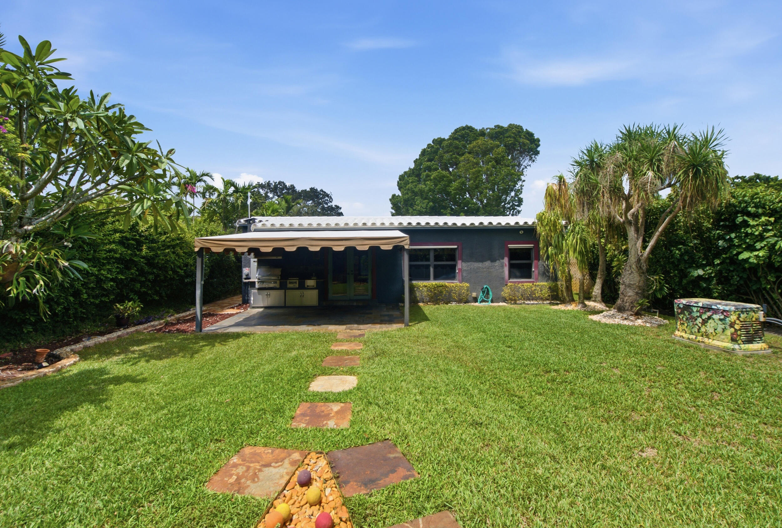 Backyard featuring a covered patio, stone paver pathway, mature tropical landscaping, and a fenced perimeter