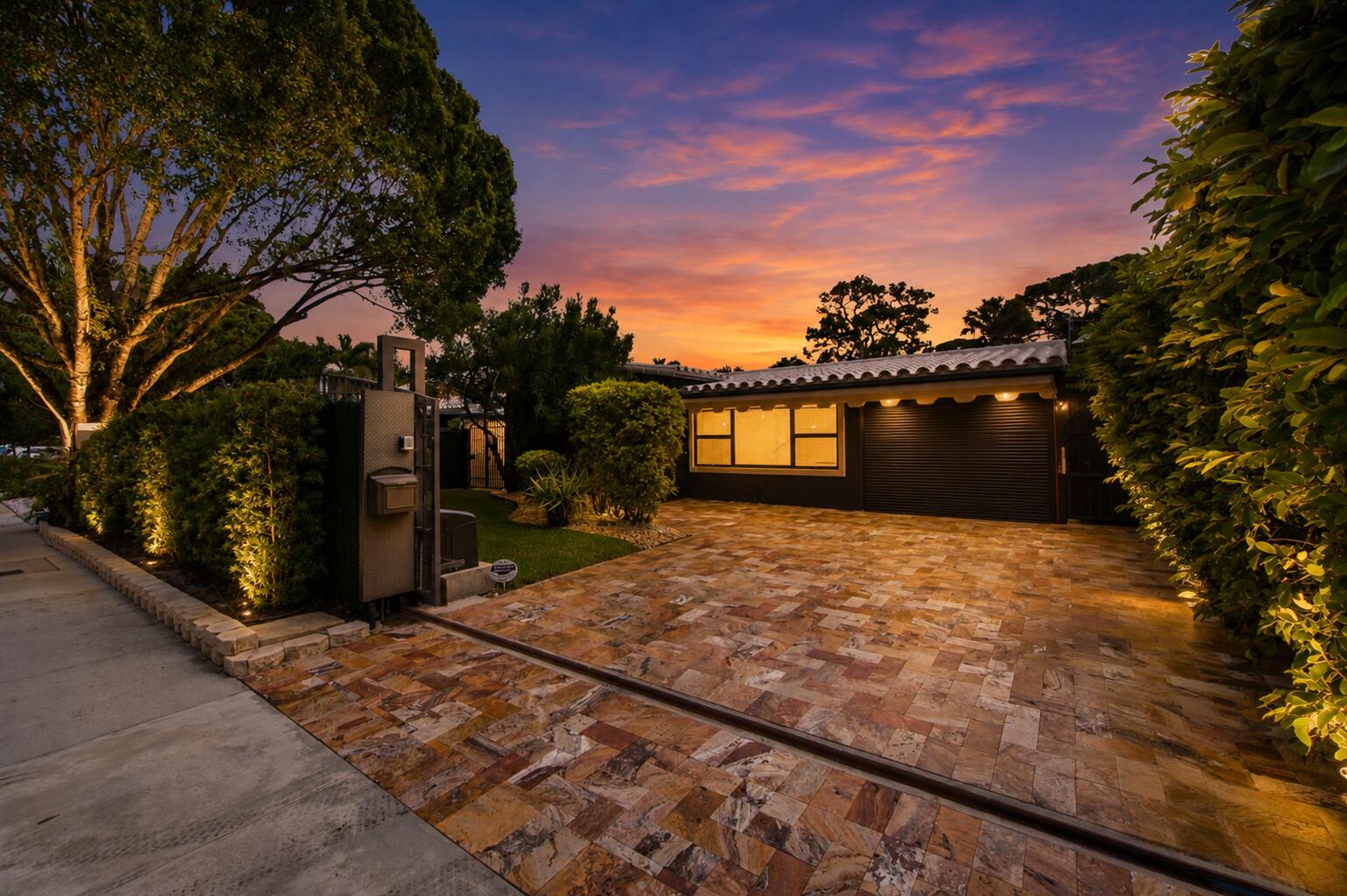 Herringbone-patterned stone driveway, gated entry, tile roofing, and integrated landscape lighting