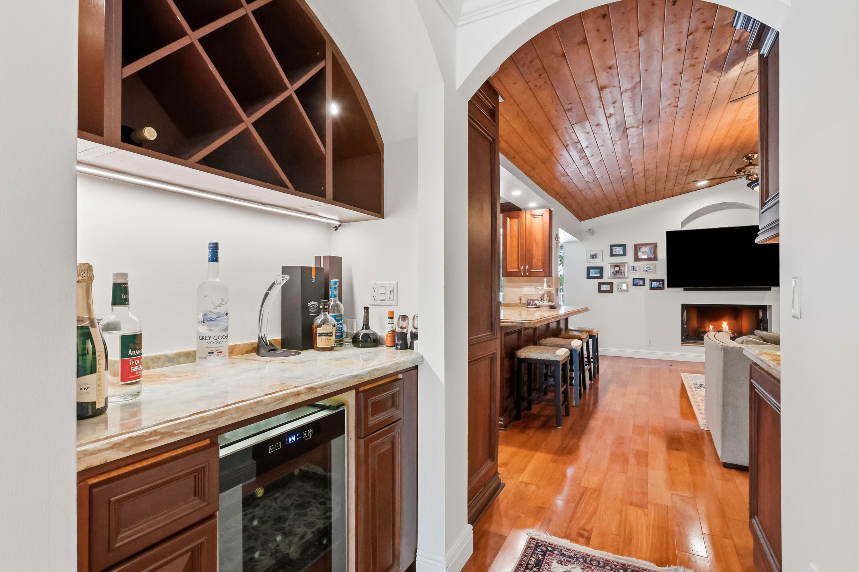 Wet bar featuring built-in cabinetry, arched wine storage, and an under-counter beverage refrigerator, highlighted by wood-finish flooring and a barrel-vaulted wood-paneled ceiling