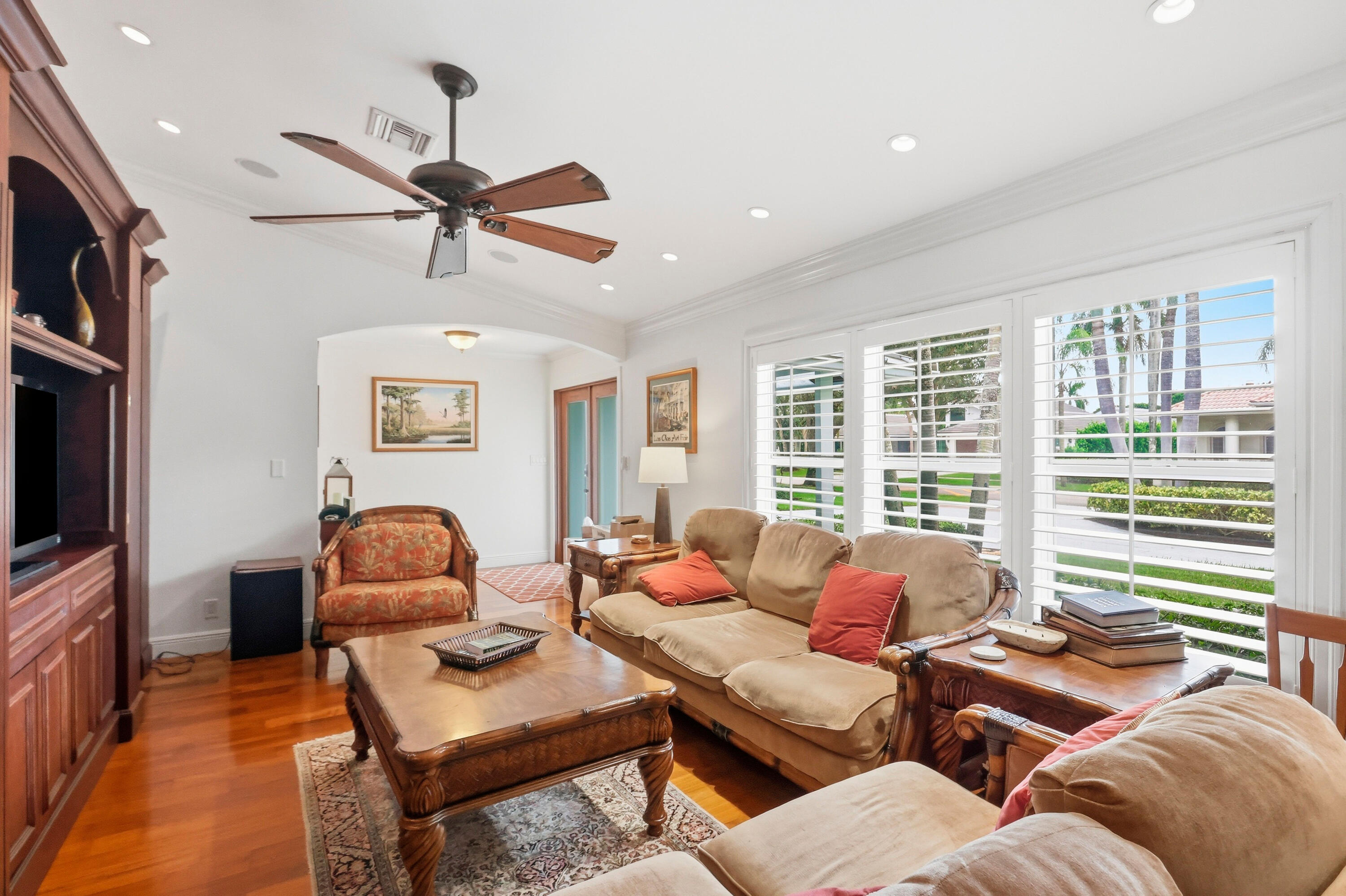 Living area featuring wood-finish flooring, recessed lighting, crown molding, plantation shutters, and built-in wooden cabinetry