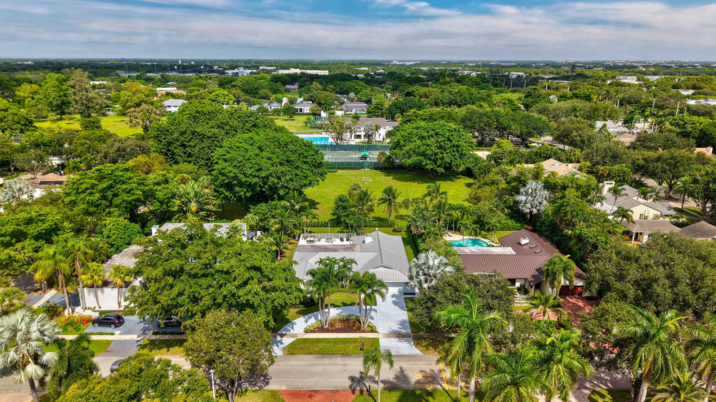 Aerial perspective of a sprawling property featuring mature canopy trees, expansive lawn space, and a private swimming pool with a screened enclosure