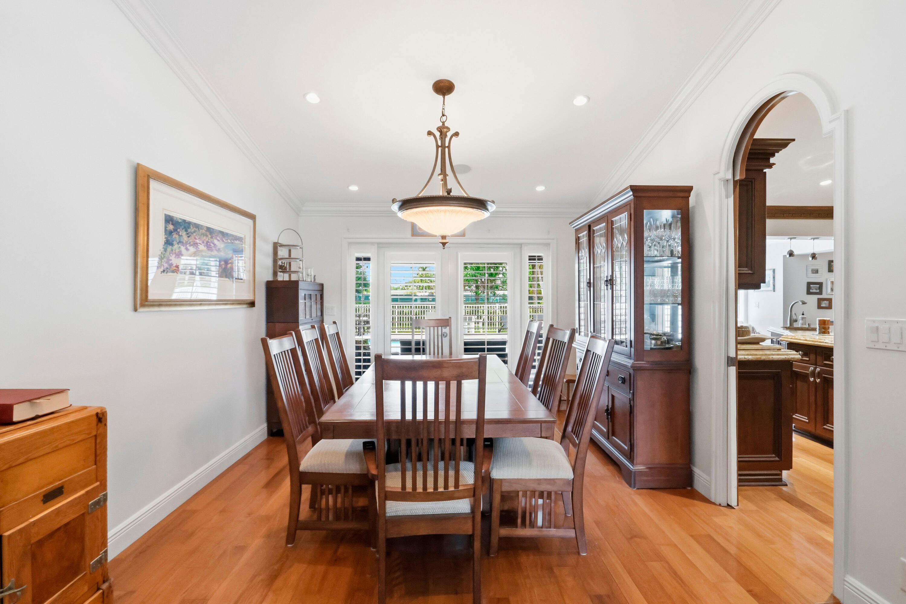 Dining area featuring wood-finish flooring, crown molding, recessed lighting, a central pendant fixture, and an arched doorway