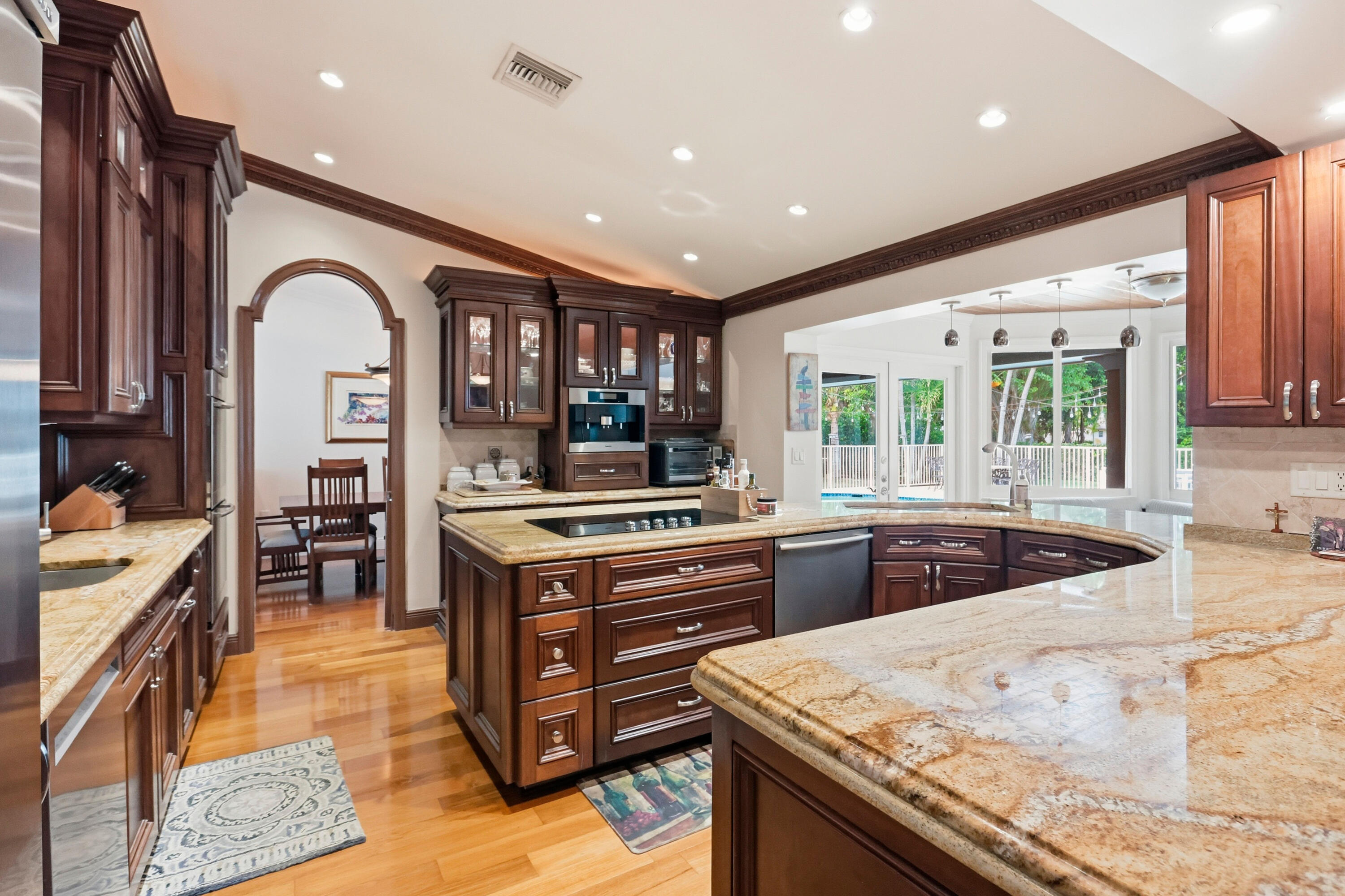Kitchen featuring wood cabinetry, stone countertops, integrated cooktop, recessed lighting, and arched doorway