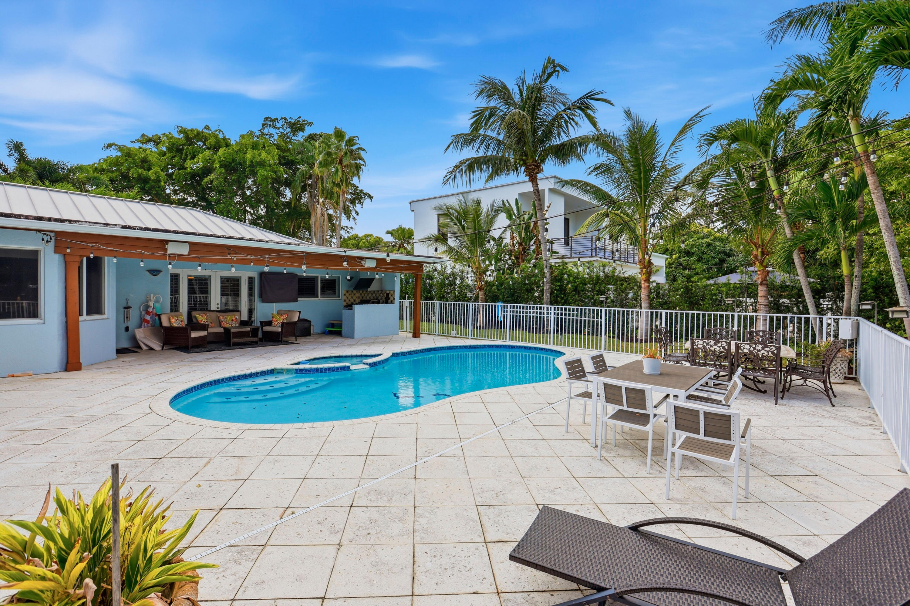 Outdoor swimming pool featuring a spillover spa, expansive paved patio, wood-post covered lanai, and white metal perimeter fencing