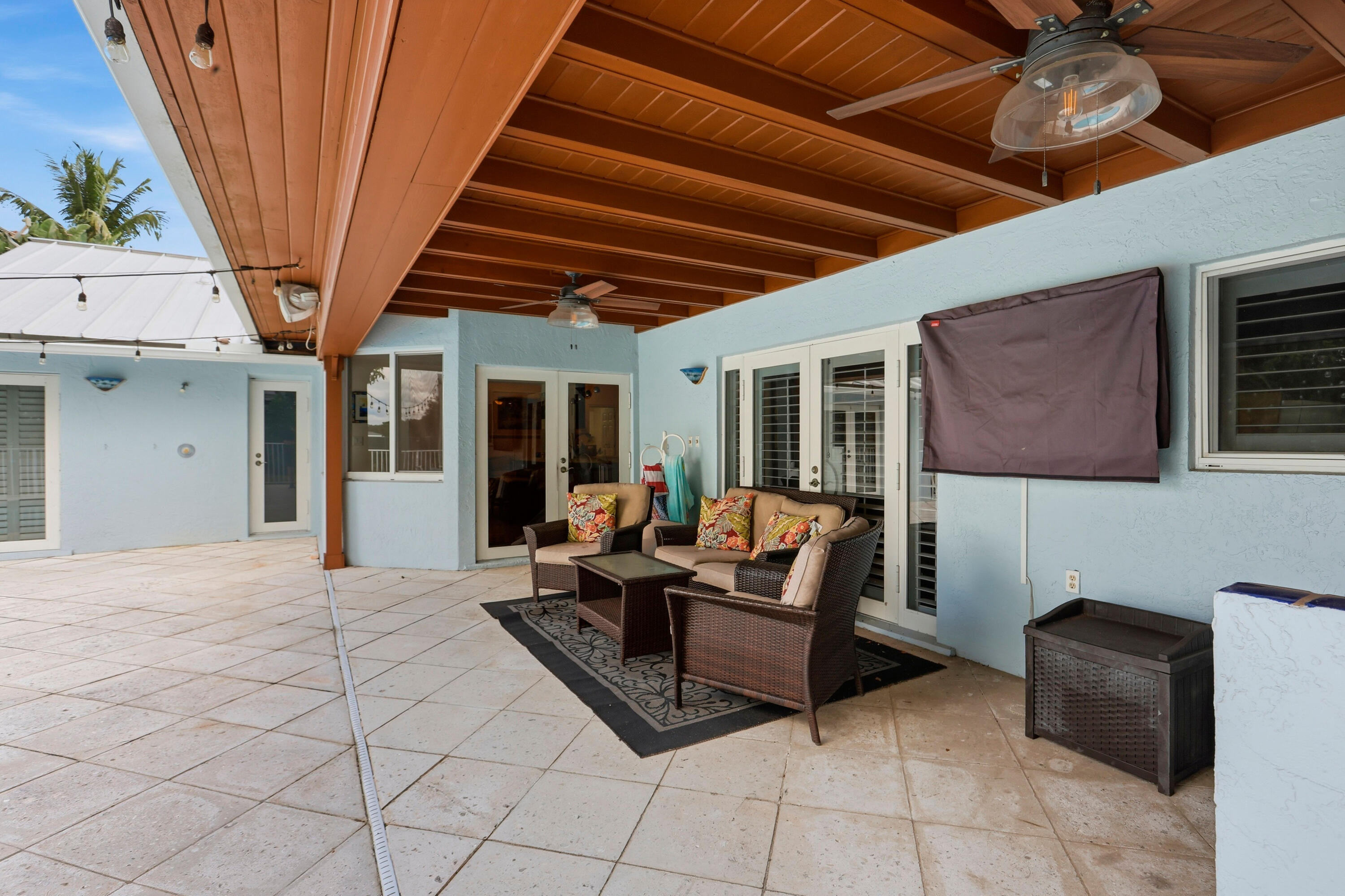Covered patio featuring a wood-beam ceiling, tiled flooring, integrated ceiling fans, and multi-panel glass entry doors