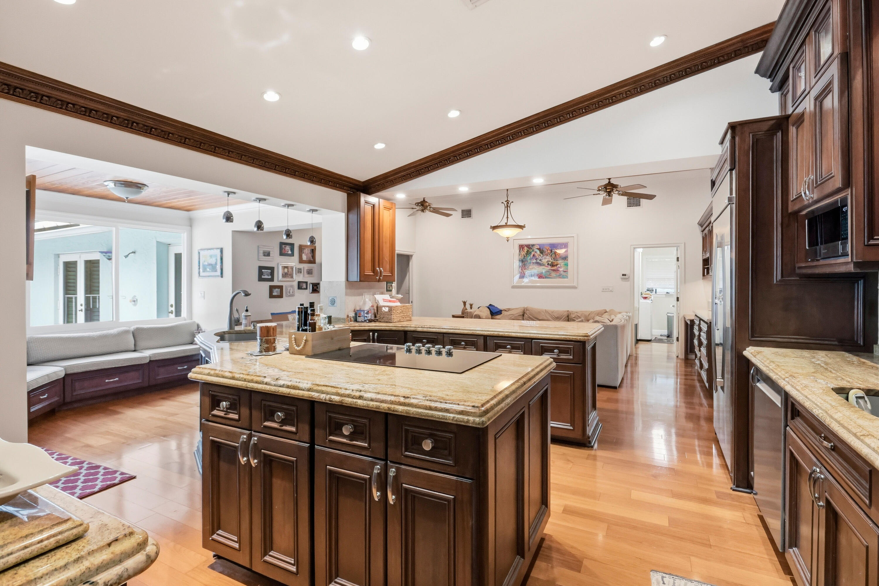 Kitchen featuring dark wood cabinetry, expansive stone countertops, an integrated cooktop on the center island, recessed ceiling lighting, and wood-finish flooring