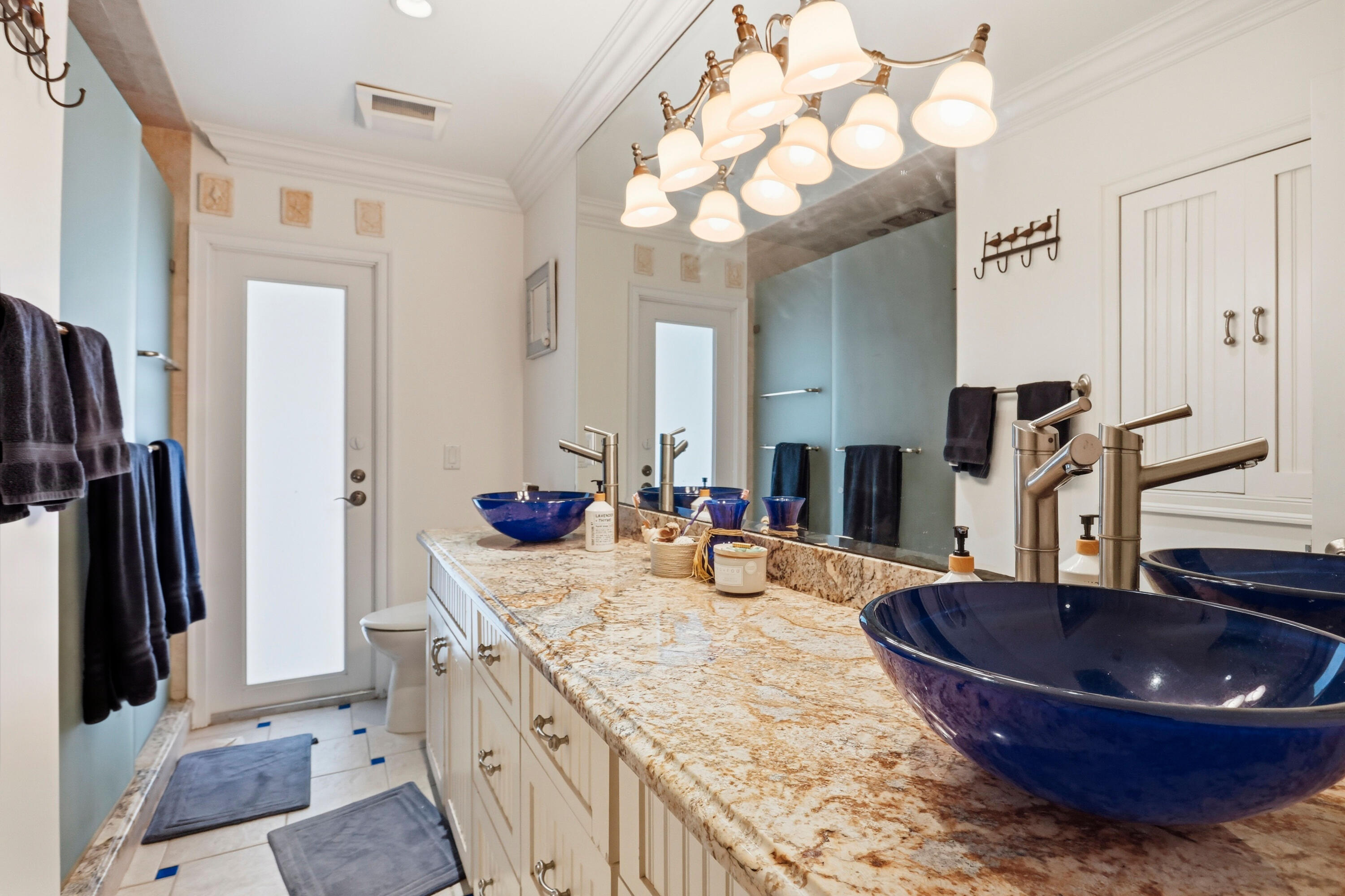Double vanity featuring stone countertops, integrated blue vessel sinks, brushed nickel fixtures, custom cabinetry, and a full-width mirror