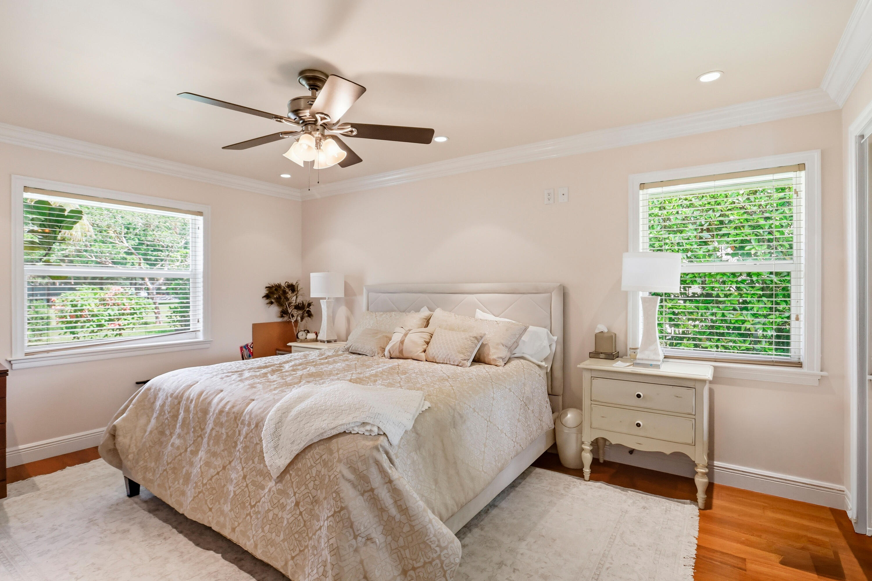 Neutral-toned room featuring crown molding, wood-finish flooring, dual windows with blinds, and a multi-blade ceiling fan with integrated light fixture