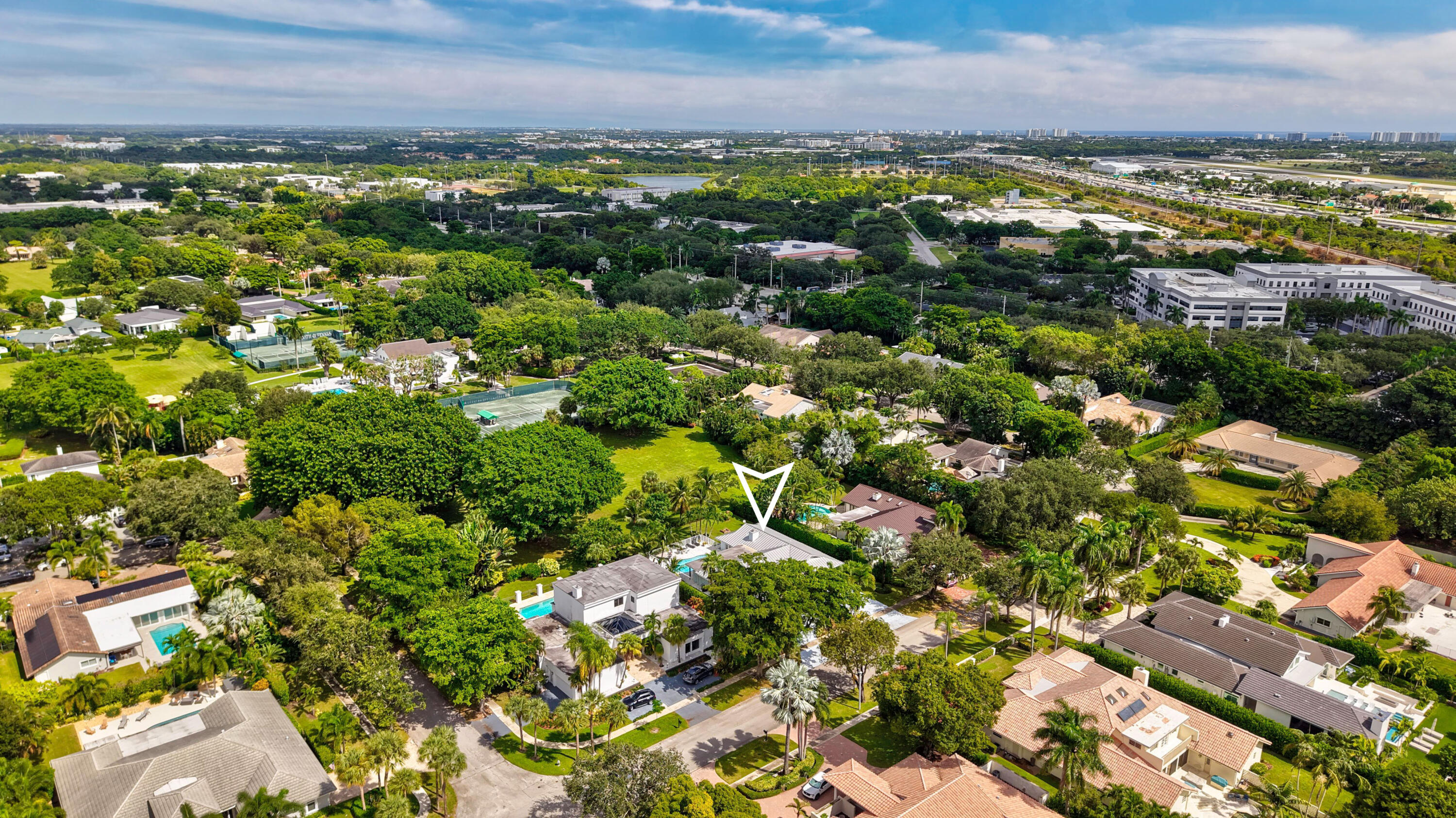 Aerial perspective of property featuring a private swimming pool, multi-level roofline, mature canopy trees, and paved driveway