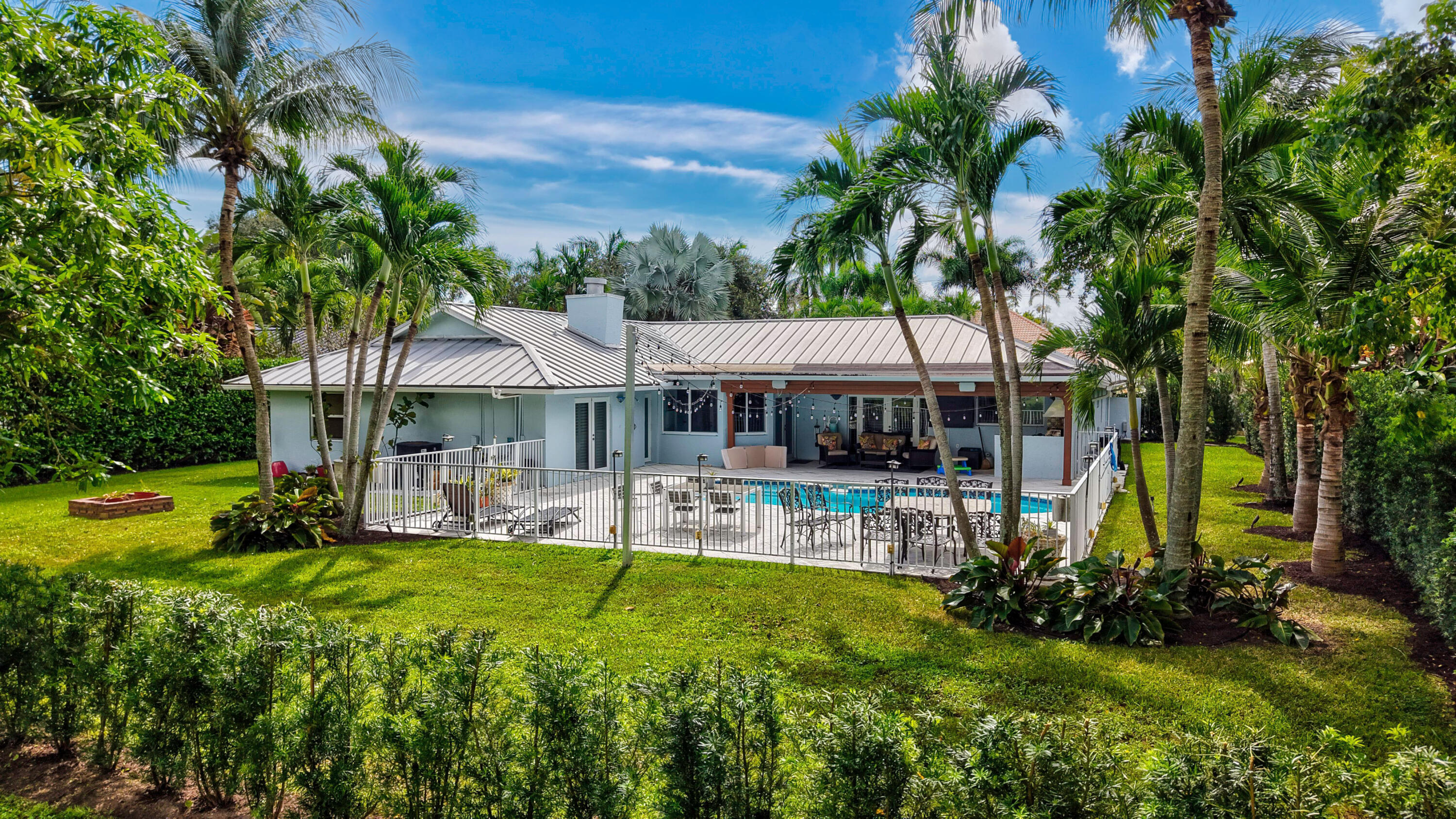 Backyard featuring a swimming pool, covered patio, metal roof, and manicured landscaping with mature palm trees