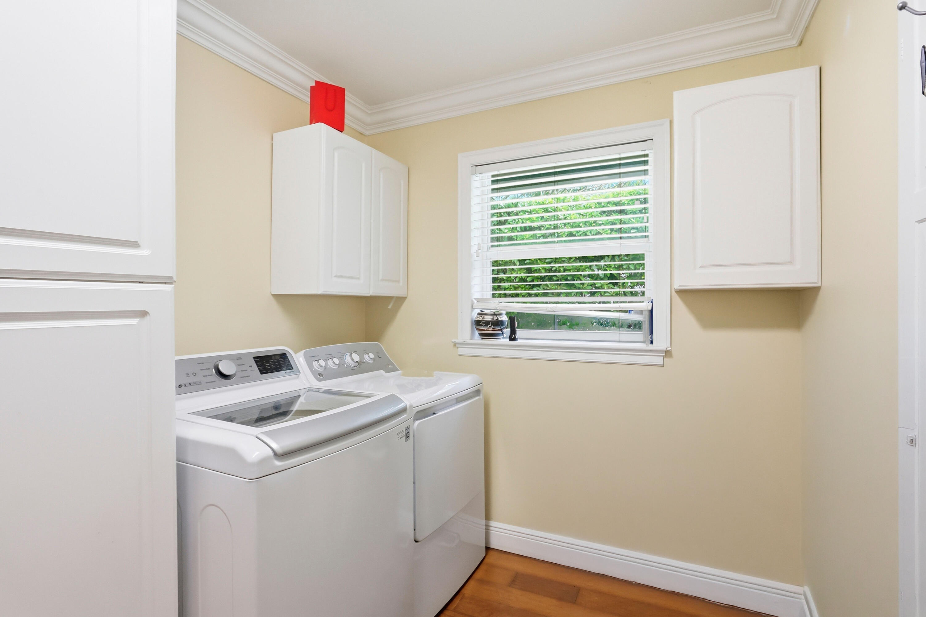 Laundry room featuring white wall-mounted cabinetry, wood-finish flooring, crown molding, and a single-hung window