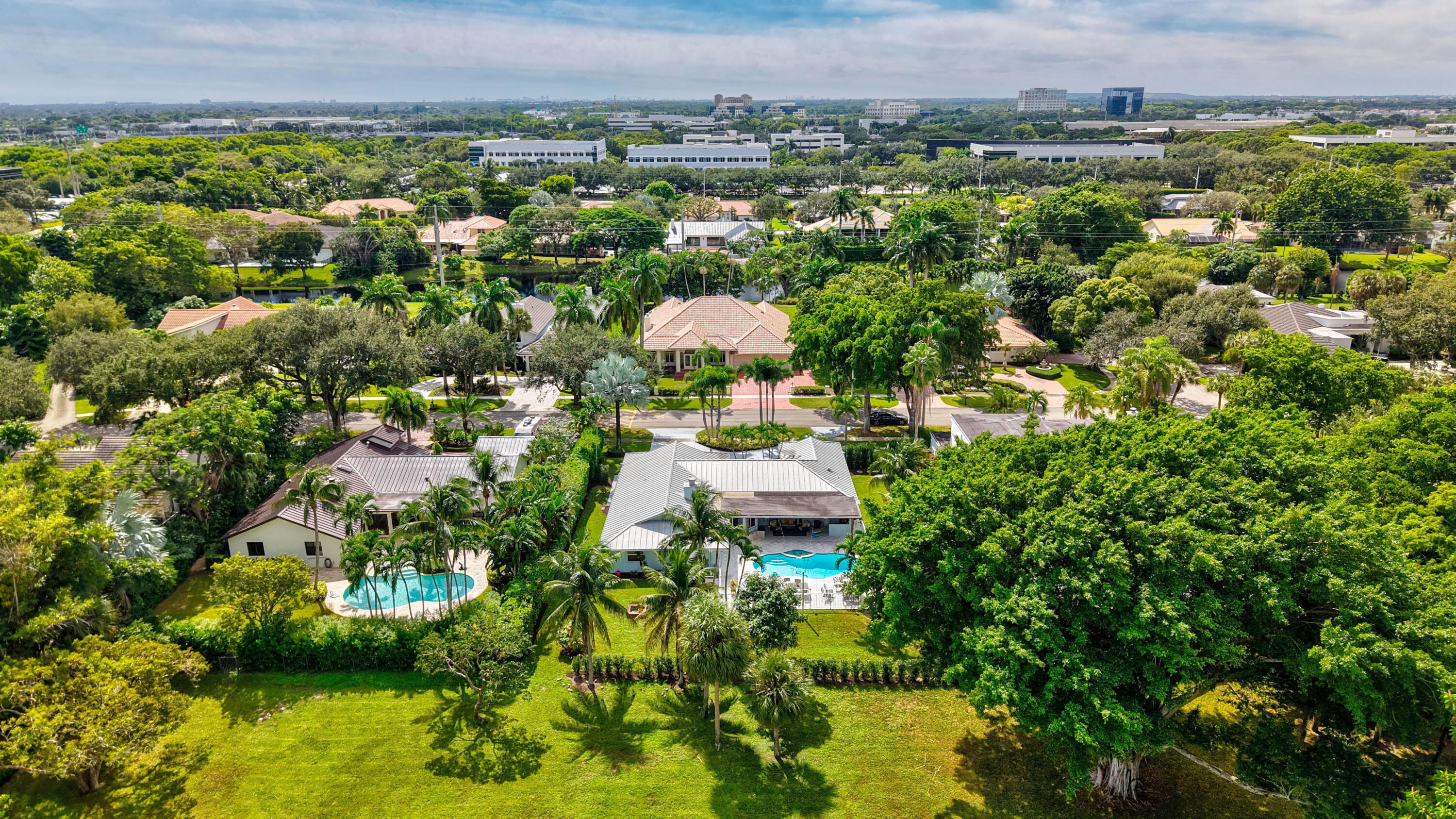 Aerial perspective featuring expansive landscaped grounds, mature canopy trees, multiple in-ground swimming pools, and residential structures with pitched roofing