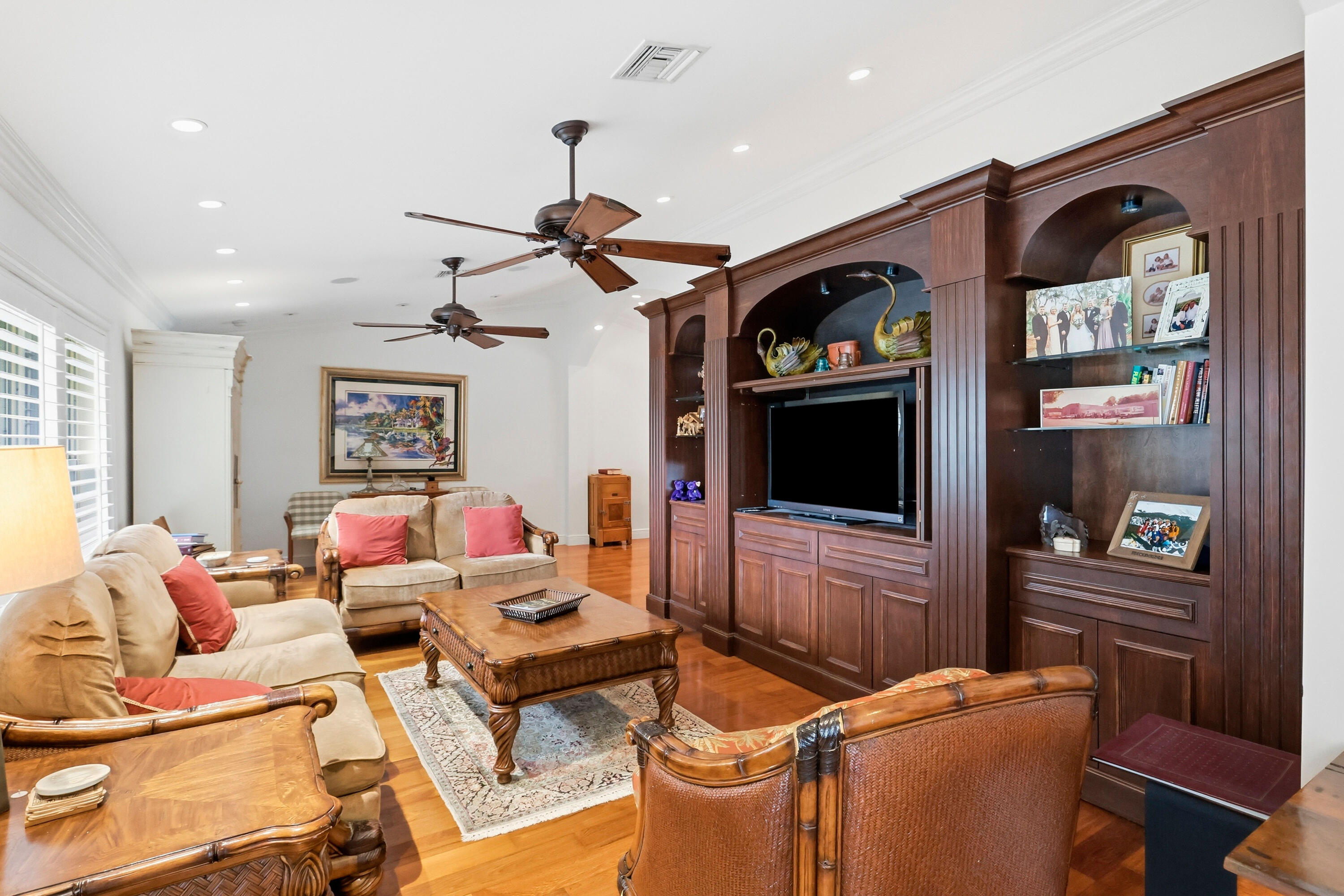 Custom wood-finish built-in cabinetry featuring arched display niches and integrated shelving, hardwood flooring, recessed ceiling lighting, and dual ceiling fans