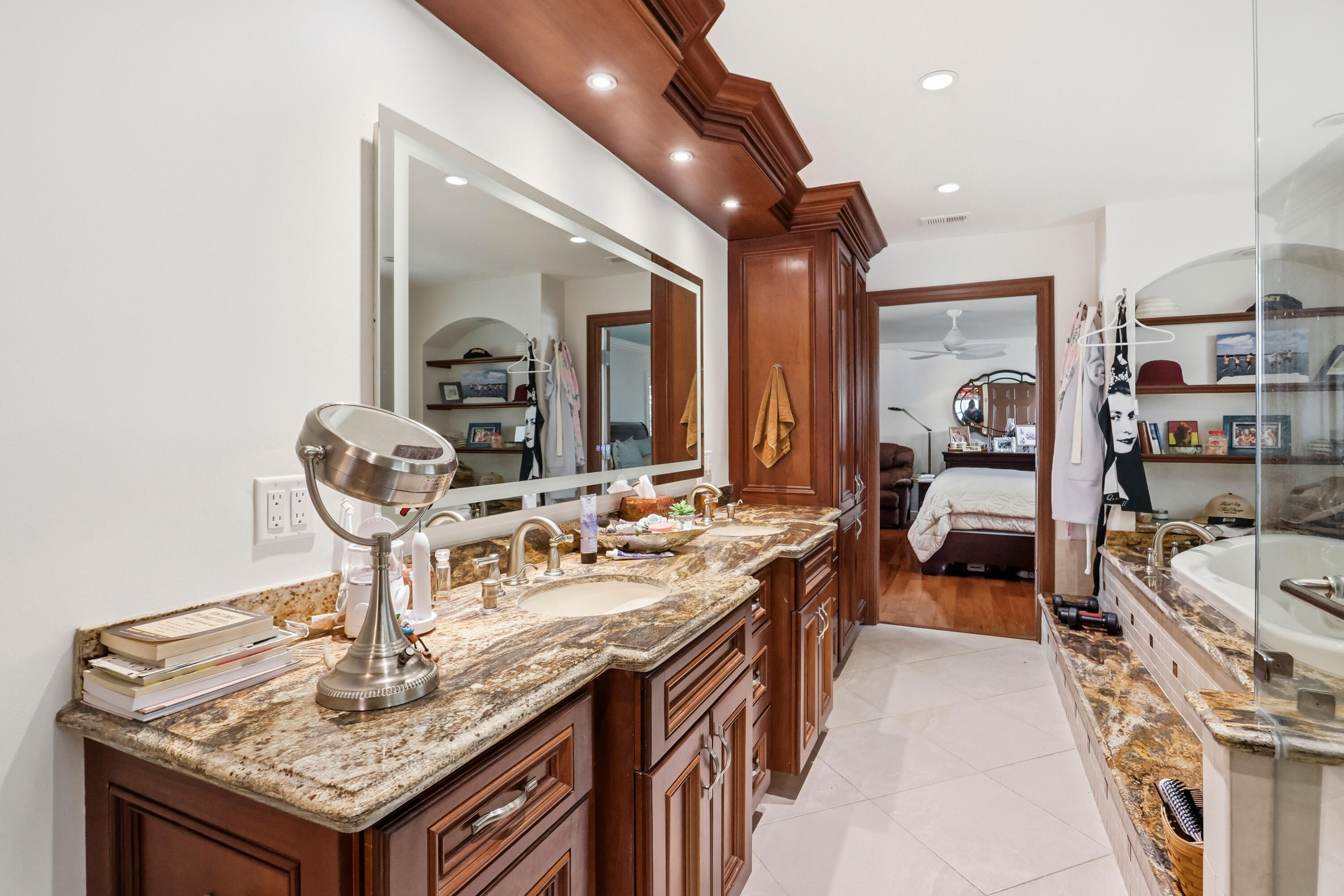 Double vanity featuring custom wood cabinetry, natural stone countertops, dual integrated sinks, and a large backlit mirror with integrated recessed lighting