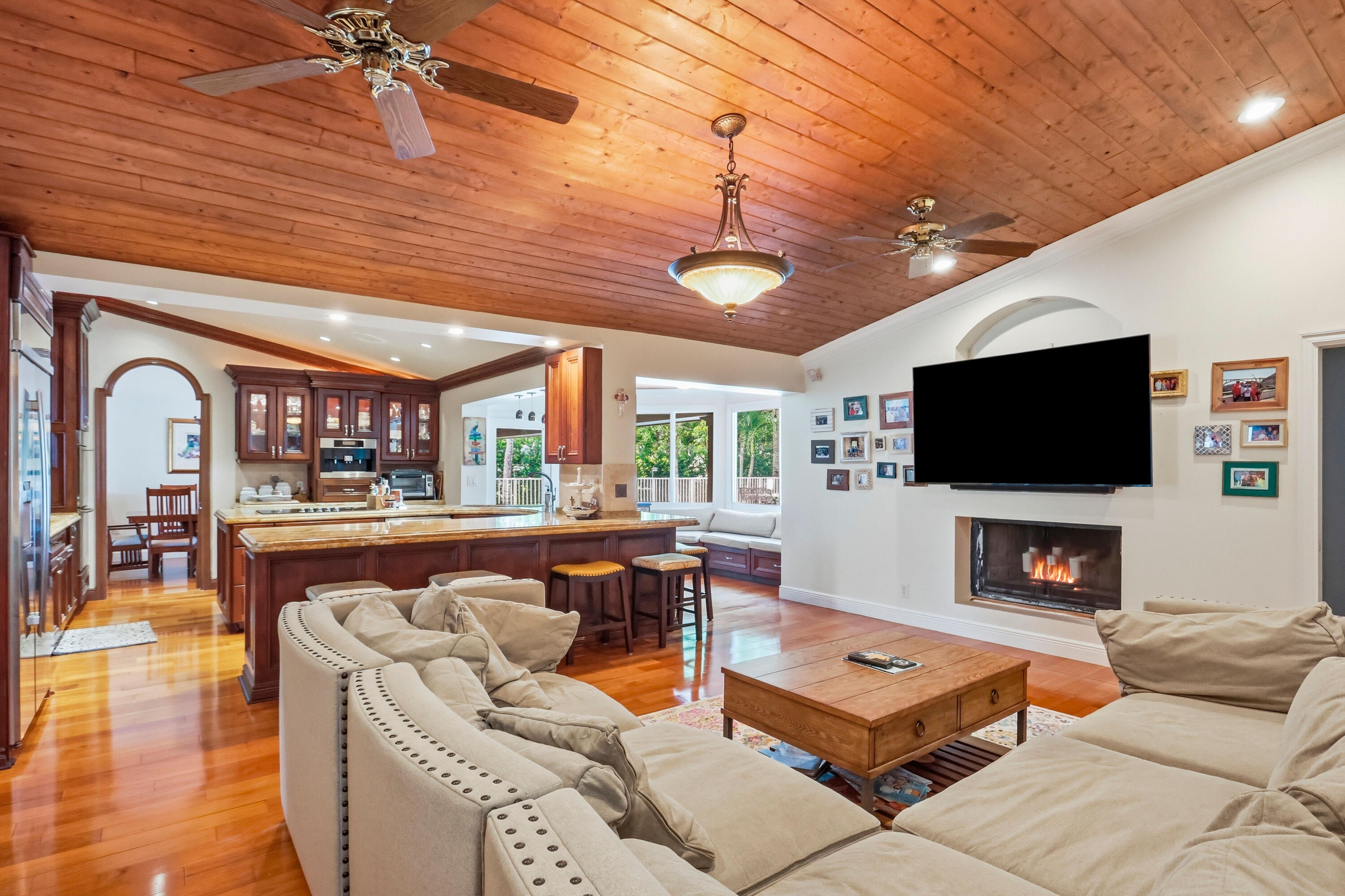 Vaulted ceiling with wood-plank finish, integrated ceiling fans, recessed lighting, and central pendant fixture