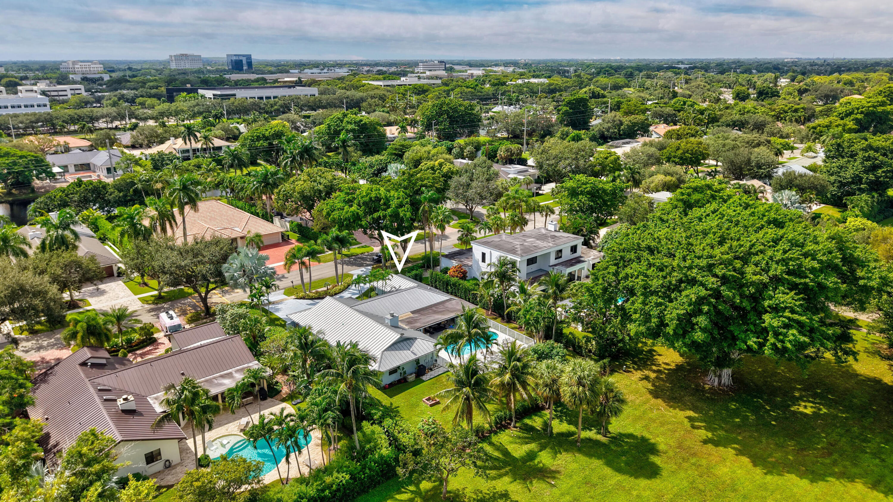 Aerial perspective featuring a single-story residence with a metal roof, an in-ground swimming pool, a concrete patio, and mature landscaping within a suburban setting