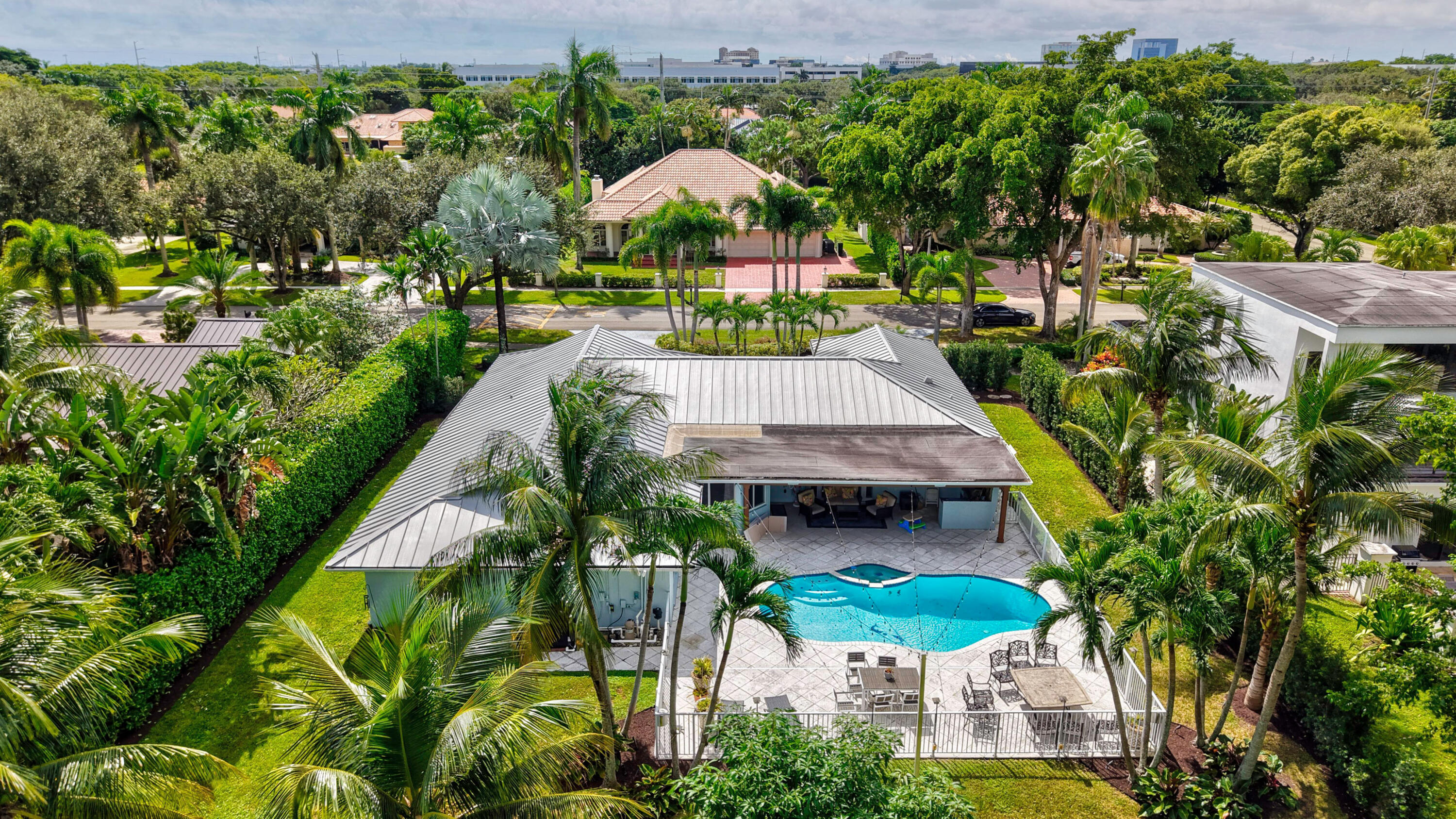 Metal roof residence featuring a swimming pool, covered patio, surrounding privacy hedges, and paved pool deck