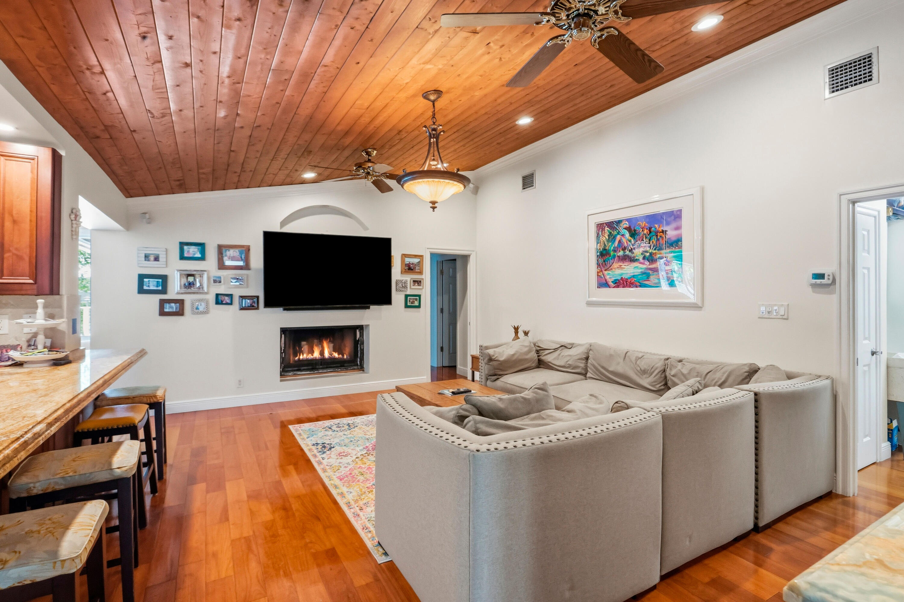 Vaulted wood-plank ceiling, wood-finish flooring, built-in fireplace, and integrated ceiling fan lighting