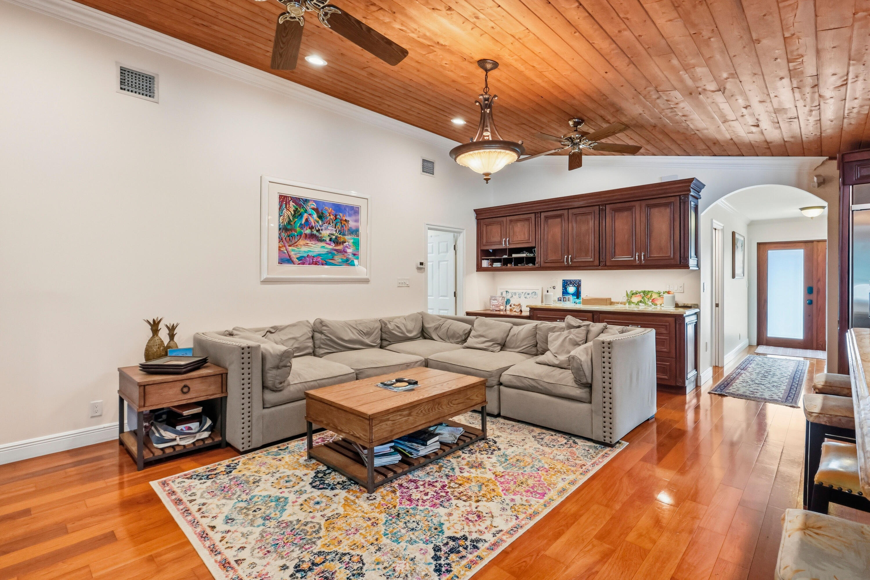 Vaulted tongue-and-groove wood ceiling featuring dual ceiling fans and a decorative chandelier, complemented by polished wood-finish flooring and built-in stained-wood cabinetry