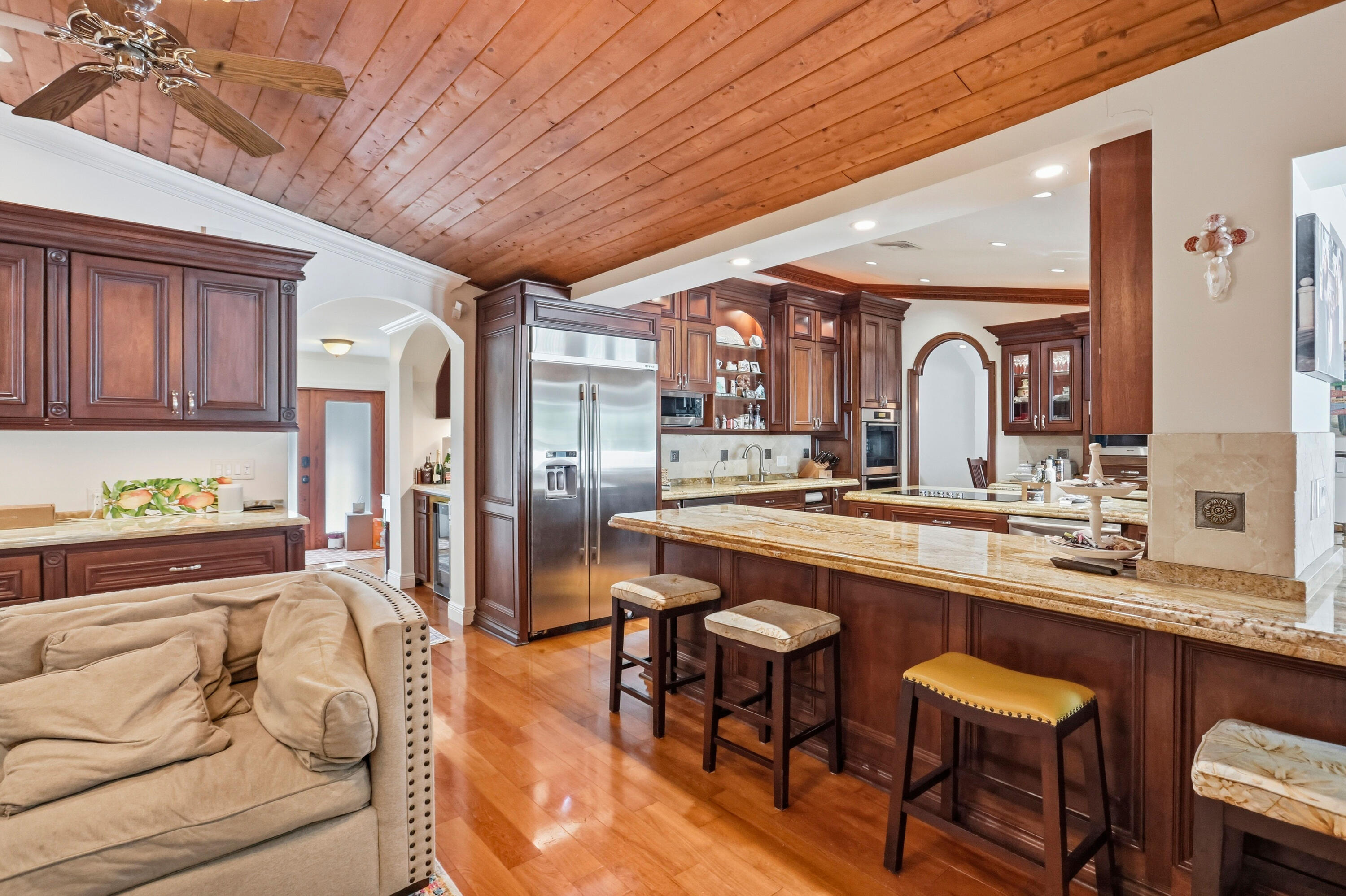 Kitchen featuring wood-plank ceiling, stained wood cabinetry, natural stone countertops, a multi-level breakfast bar, and wood-finish flooring