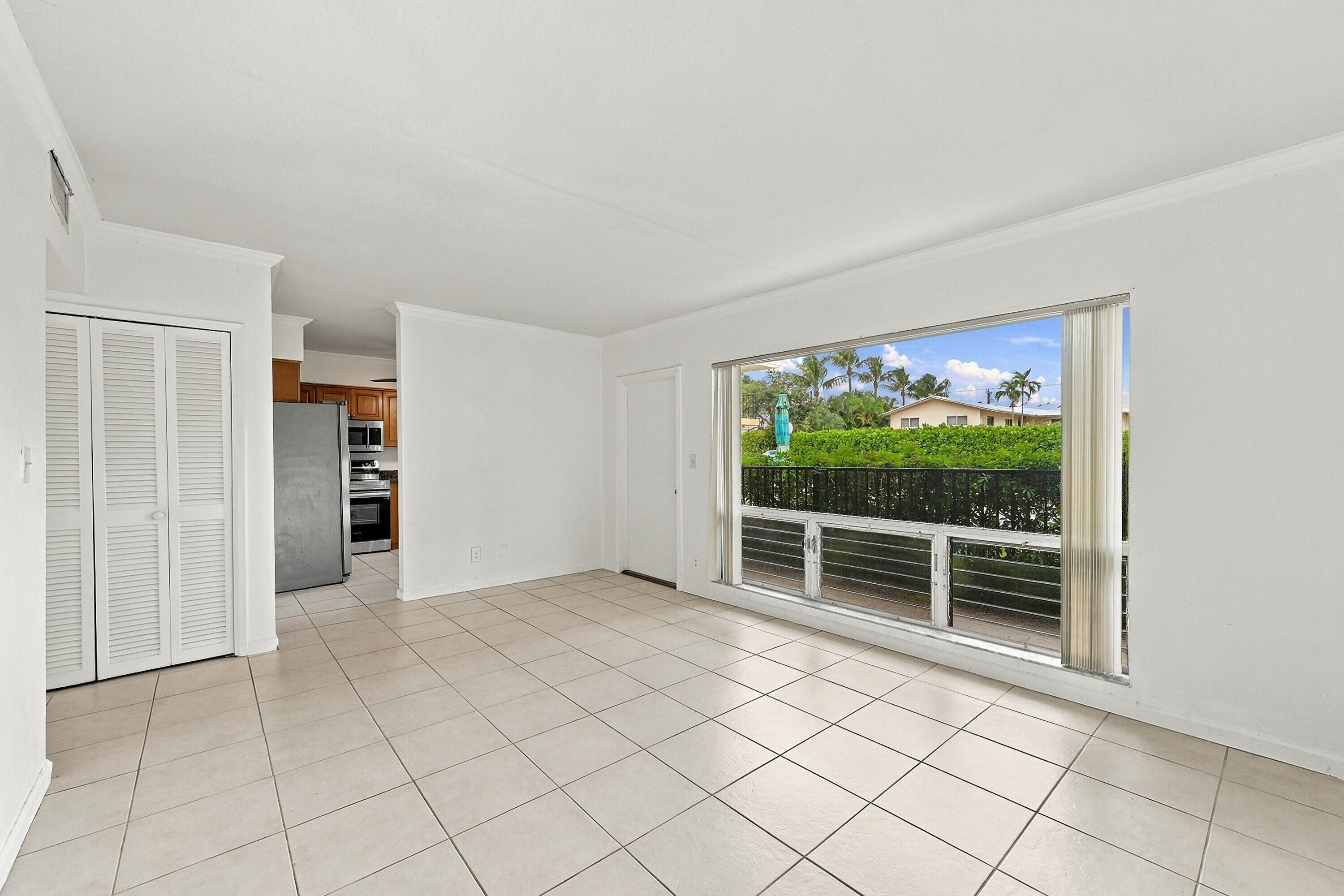 Living area featuring large-format ceramic tile flooring, floor-to-ceiling windows, and built-in louvered closet doors