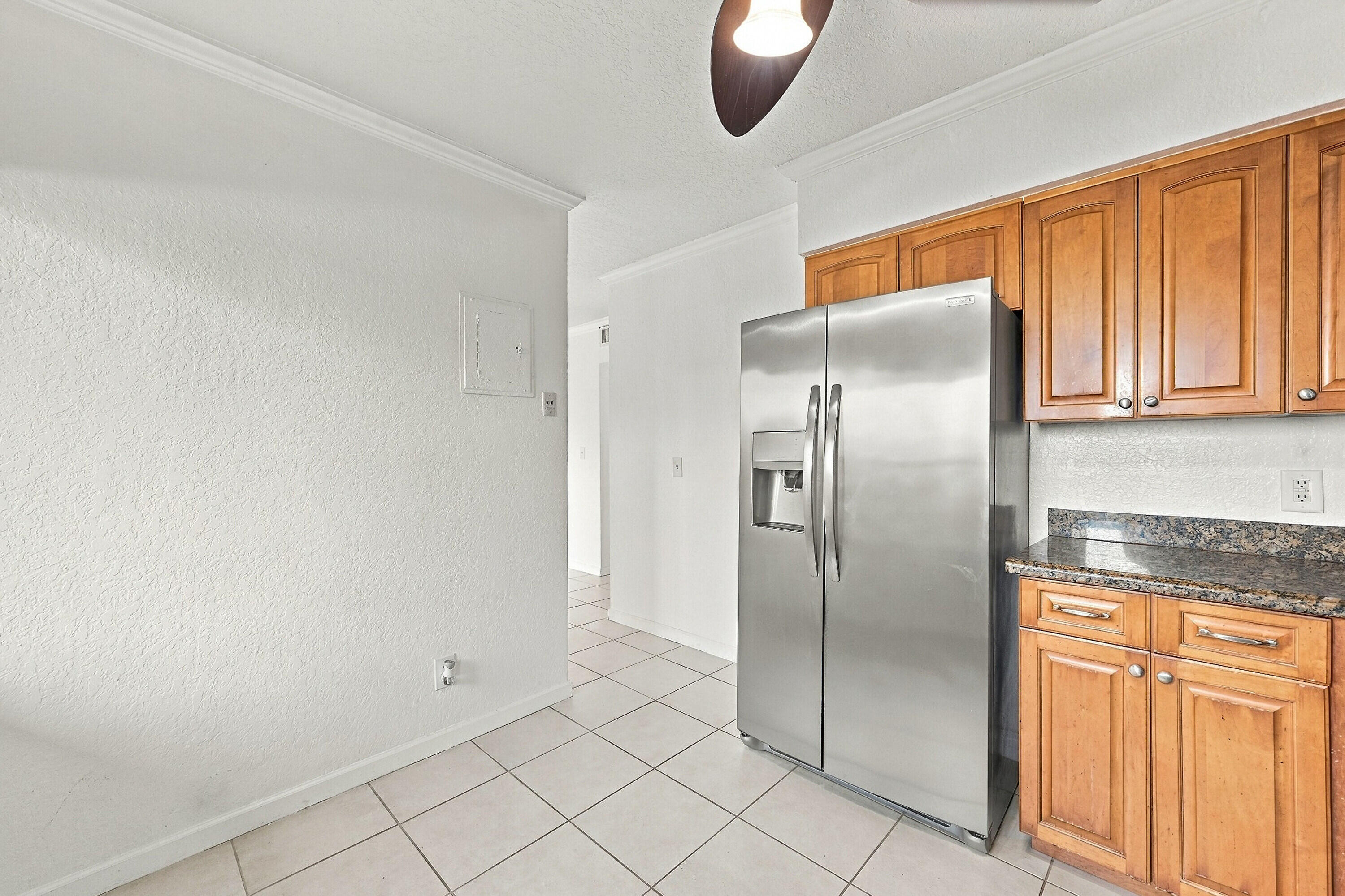 Kitchen area featuring wood cabinetry, stone-finish countertops, stainless steel side-by-side refrigerator, and tile flooring