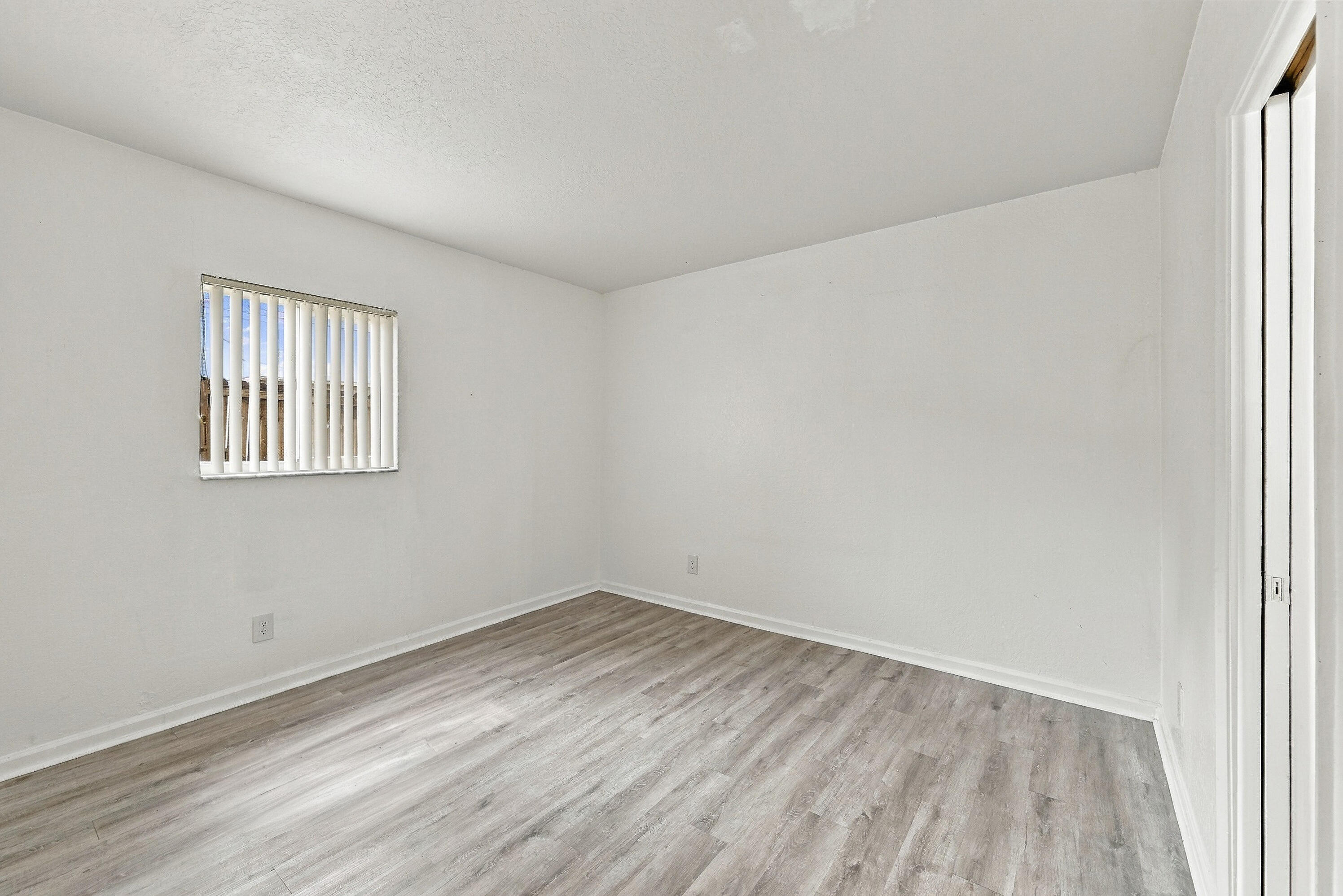 Neutral interior featuring wood-finish flooring, white walls, and a single-pane window with vertical blinds