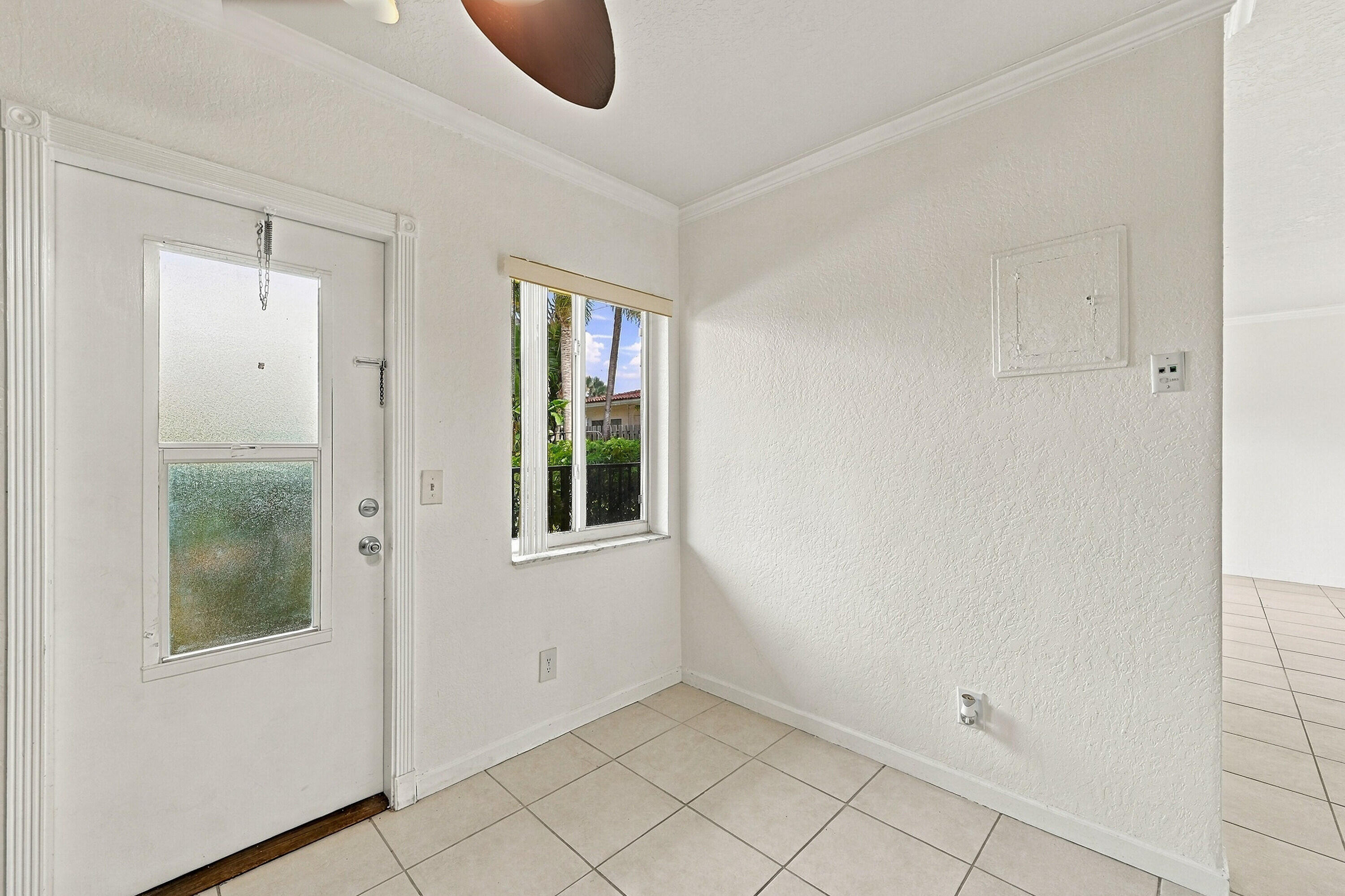Entryway featuring neutral tile flooring, textured wall finishes, crown molding, and a door with an integrated window panel