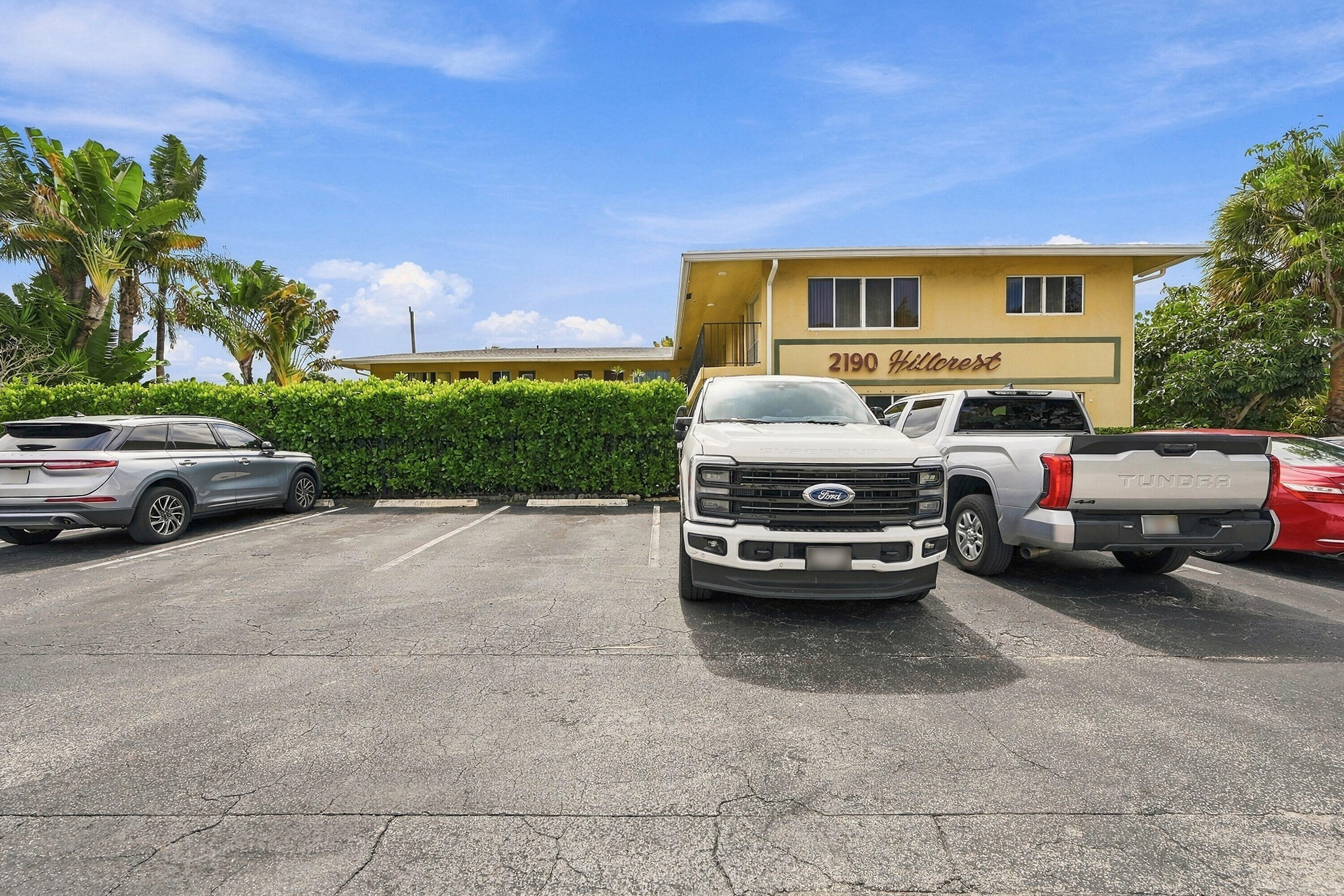 Multi-unit exterior featuring paved surface parking and manicured perimeter hedges