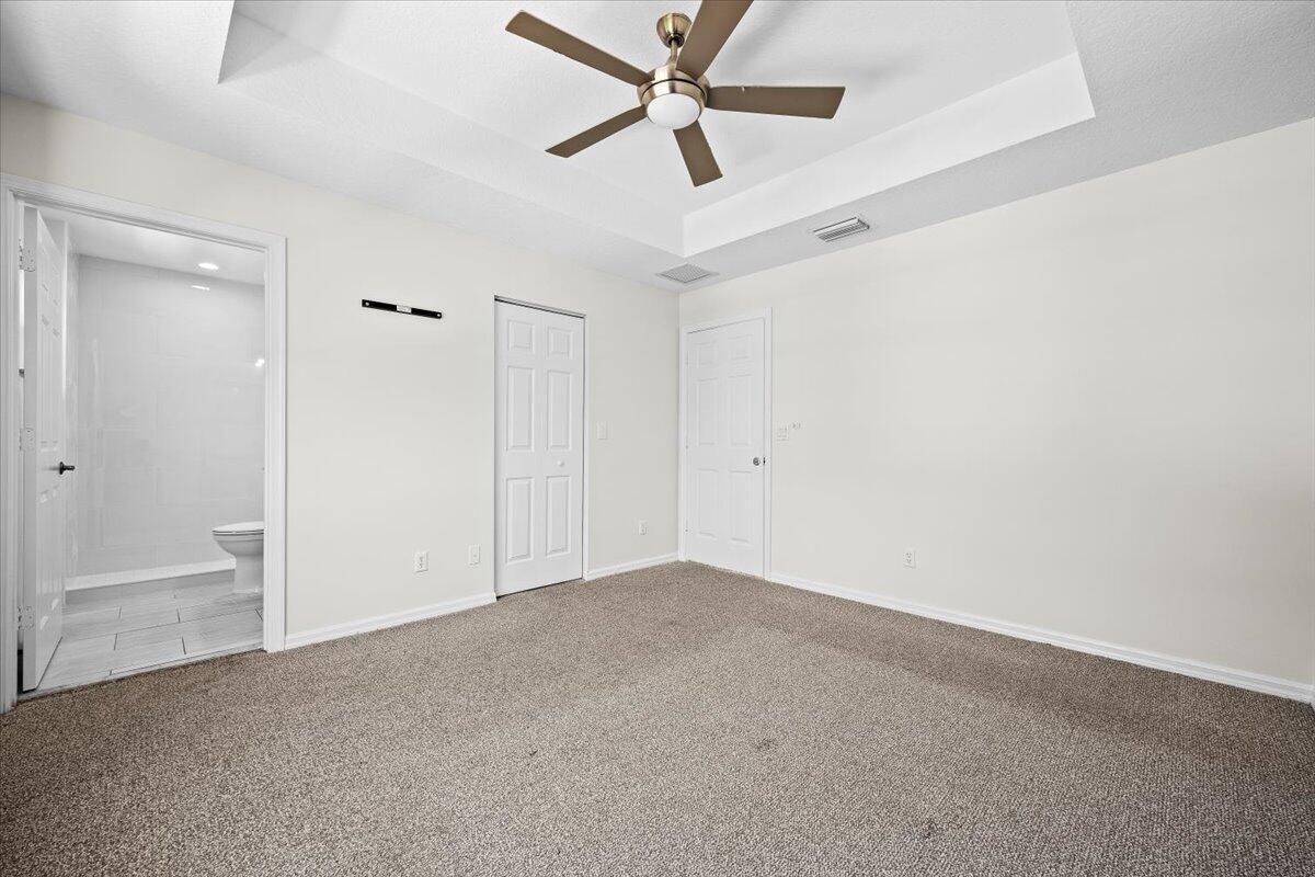 Additional view of the primary suite highlighting the tray ceiling, generous floor space, and access to the bathroom.