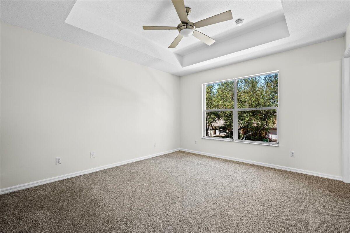 Spacious primary suite with a tray ceiling, ceiling fan, and natural light.