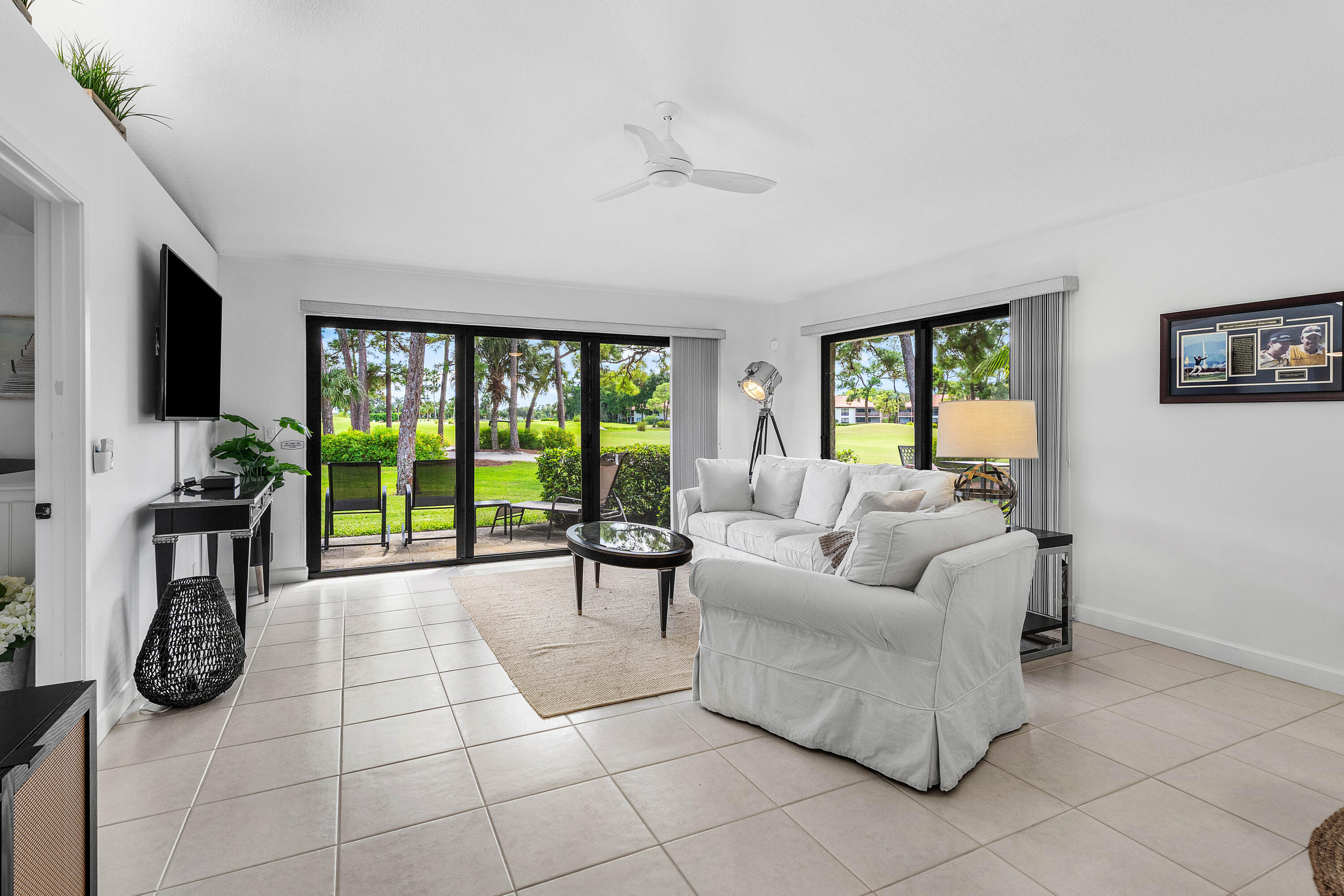 Living area featuring large-format neutral tile flooring, expansive sliding glass doors, and a ceiling-mounted fan