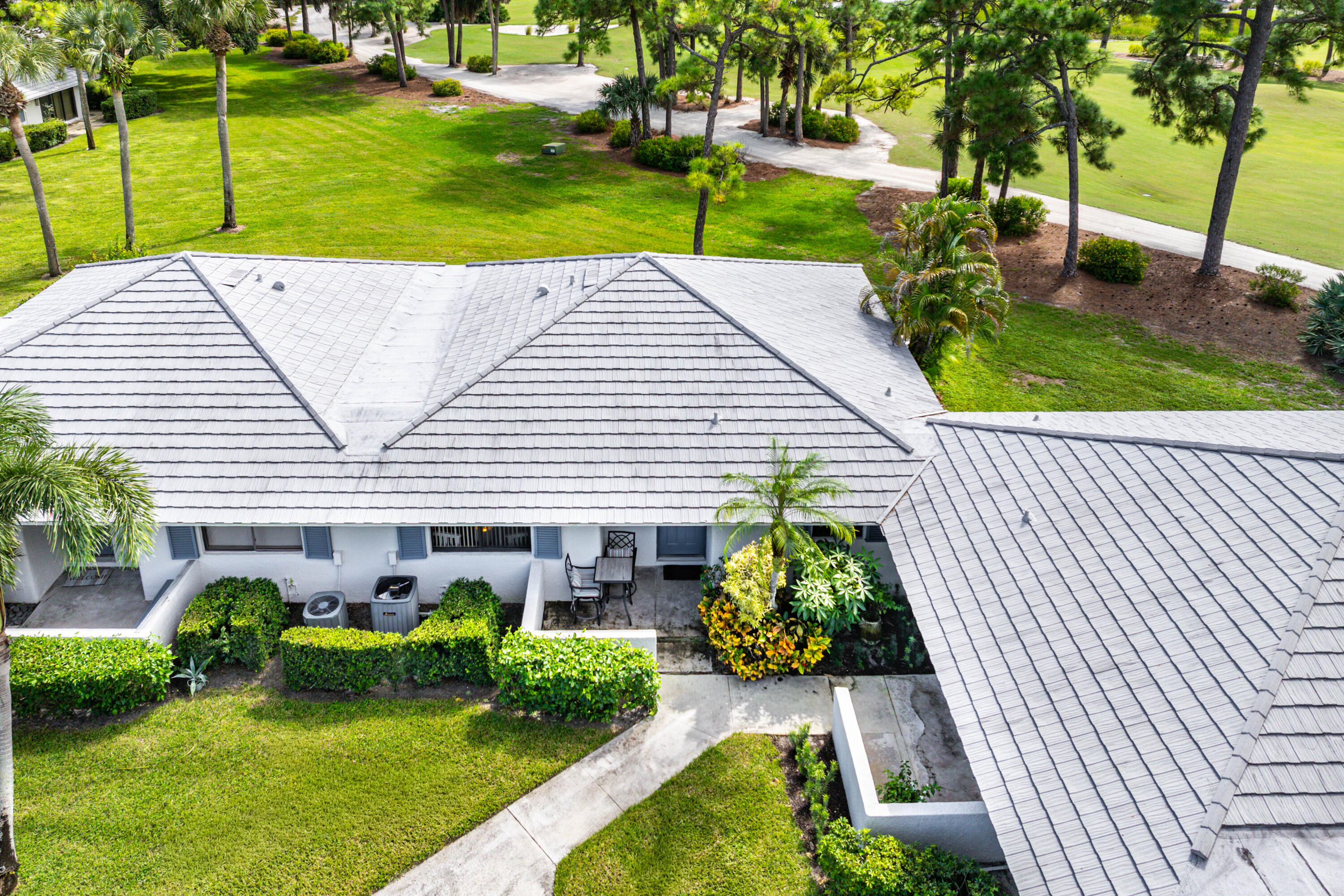Exterior perspective featuring a multi-gabled tile roof, manicured lawn, established landscaping, and paved outdoor patio area
