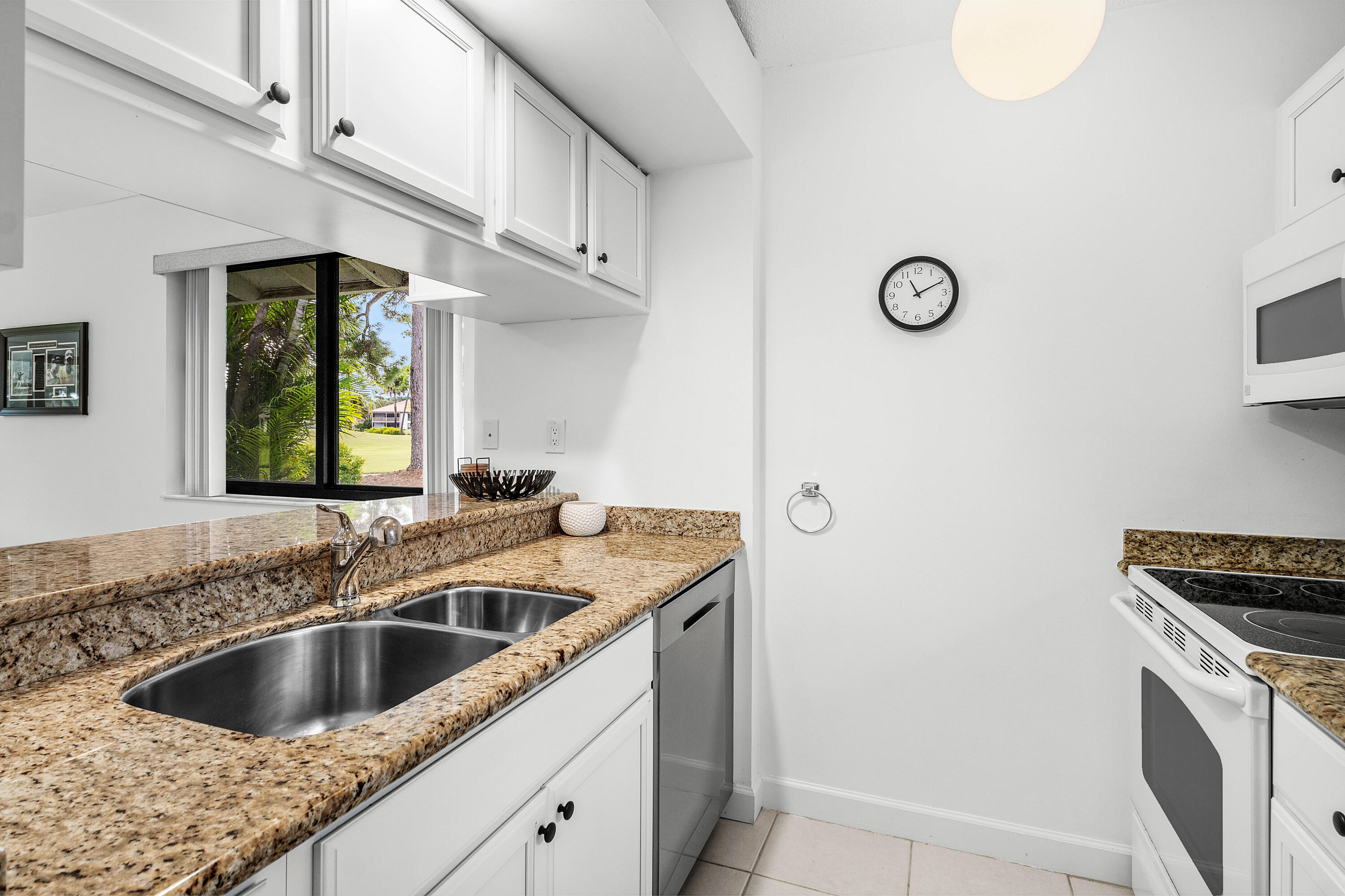 Kitchen featuring white shaker-style cabinetry, stone countertops, dual-basin stainless steel sink with a high-arch faucet, integrated stainless steel dishwasher, and built-in white electric range with overhead microwave