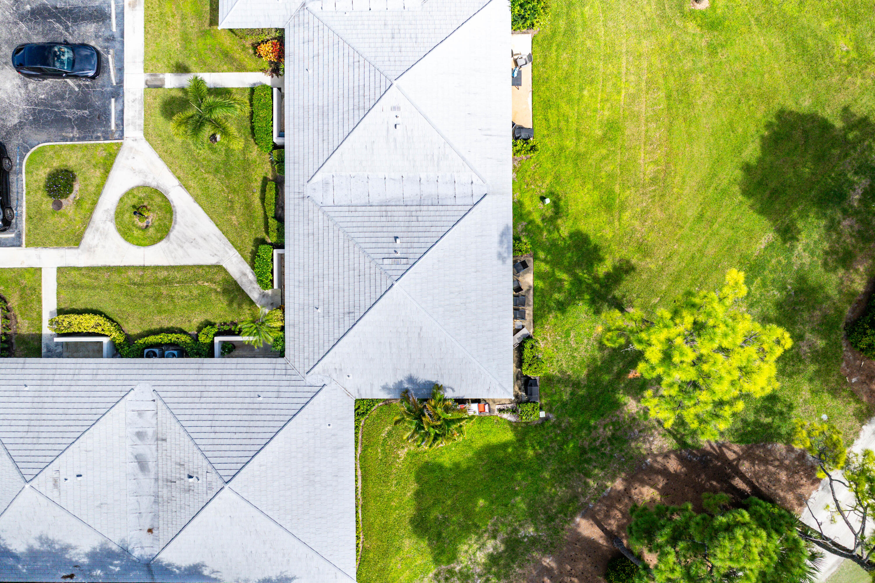 Aerial perspective of property featuring a hip roof, concrete paved walkways, expansive manicured lawn, and mature trees