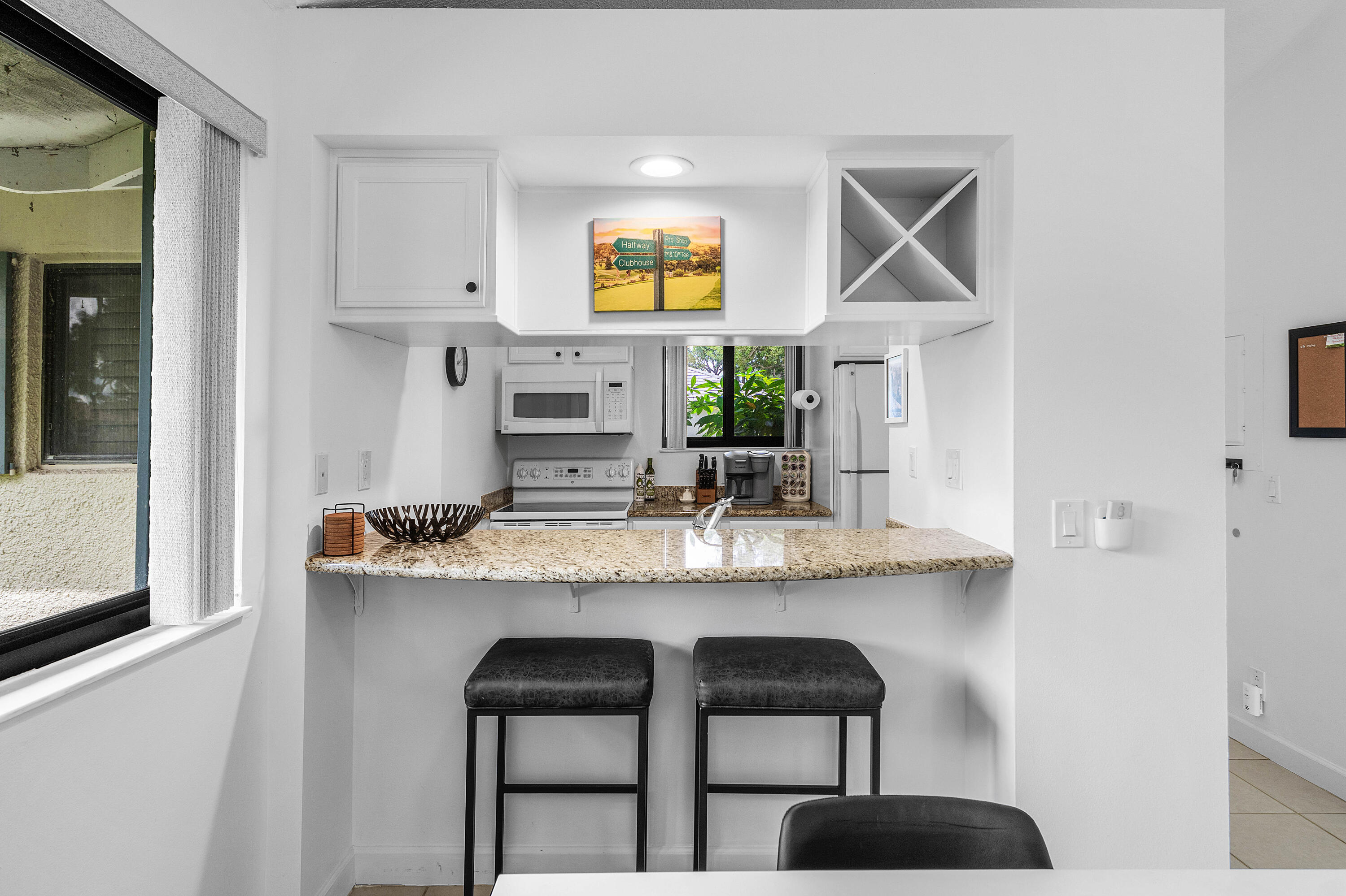 Kitchen featuring a stone countertop breakfast bar, custom cabinetry including built-in wine storage, recessed lighting, and a white built-in microwave