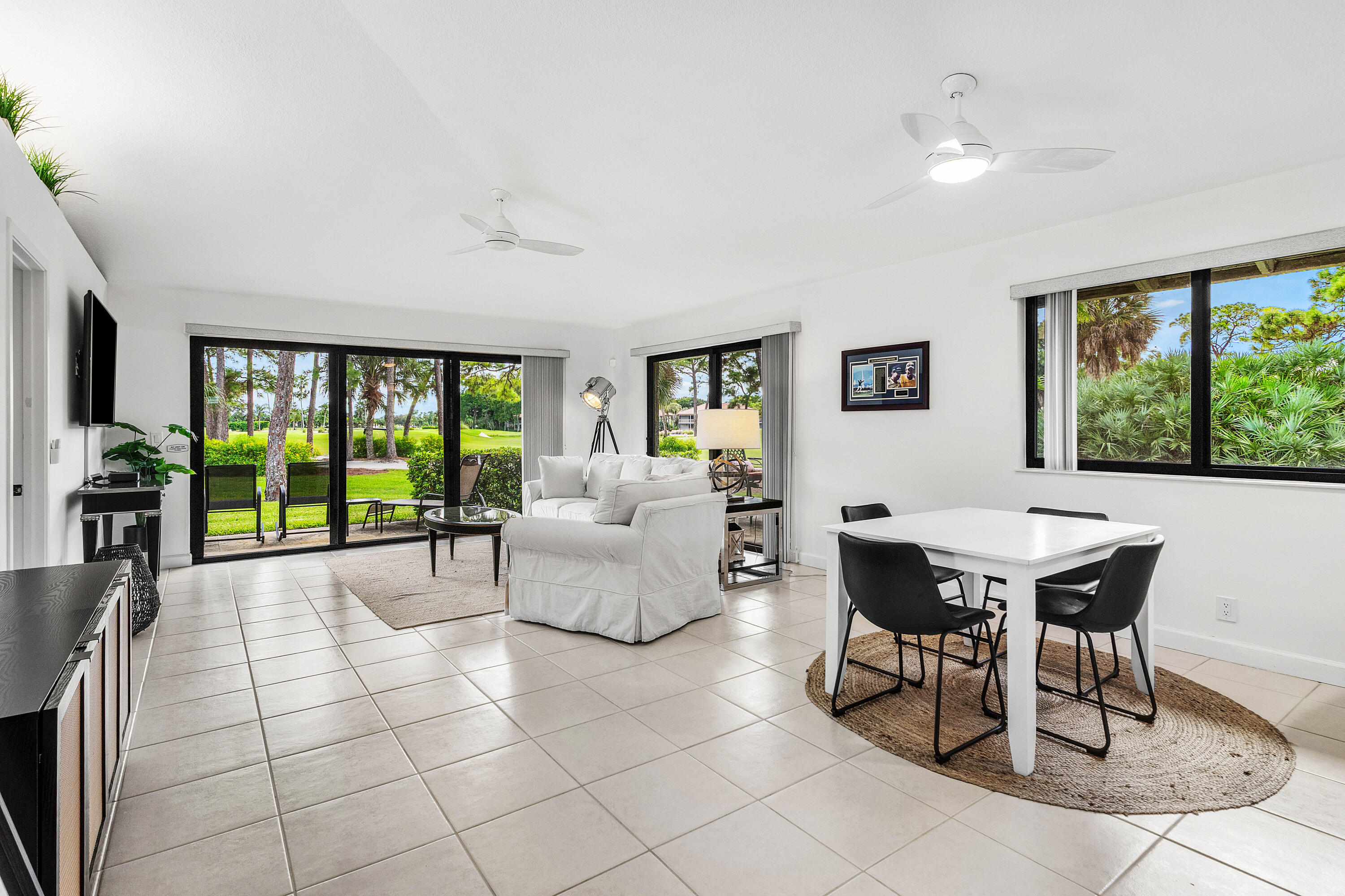 Open-concept interior featuring large-format ceramic tile flooring, expansive sliding glass doors, black-framed windows, and dual ceiling fans