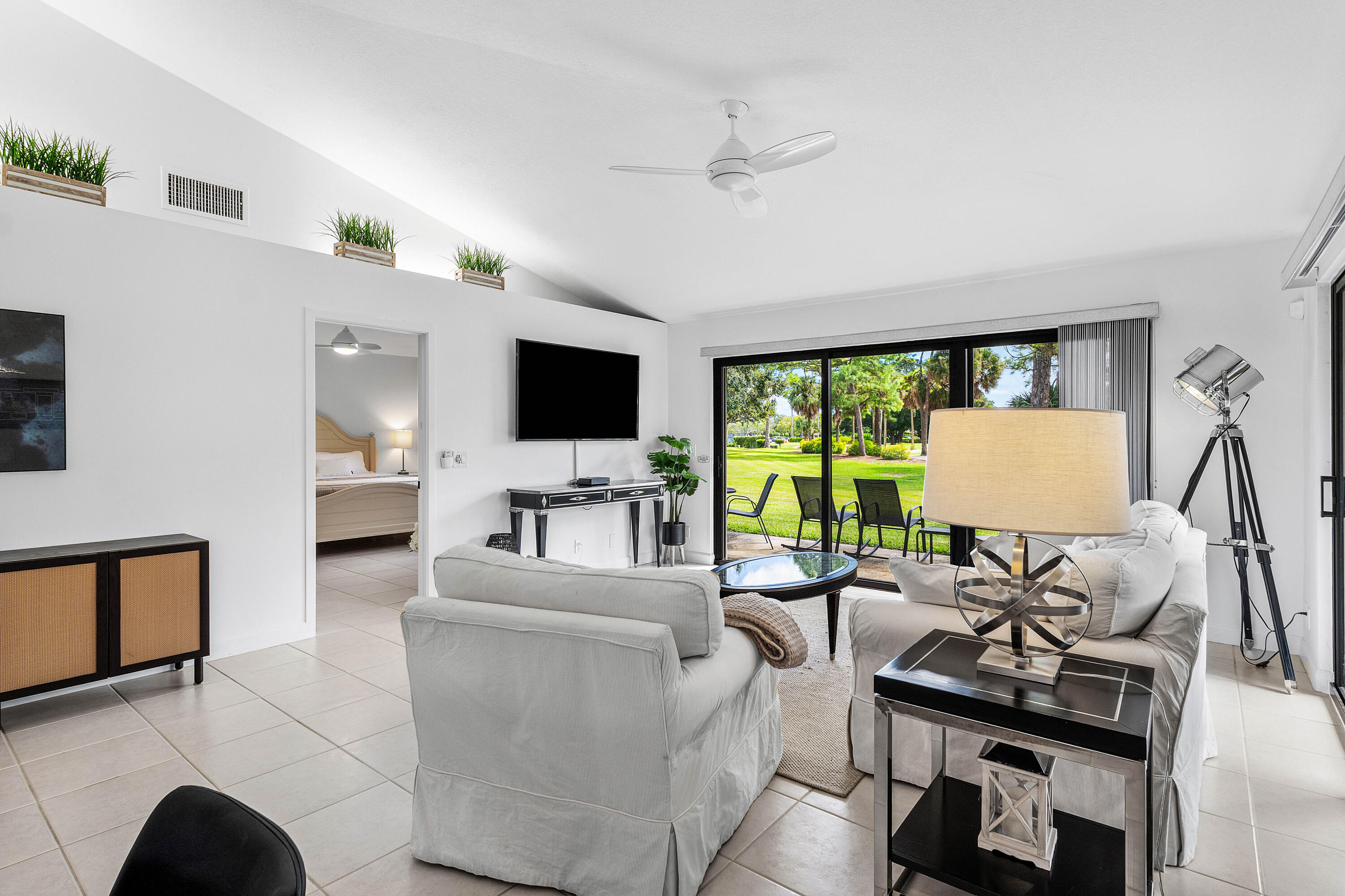 Vaulted ceiling featuring a central cooling fan and large-format tile flooring, highlighted by sliding glass doors opening to outdoor green space