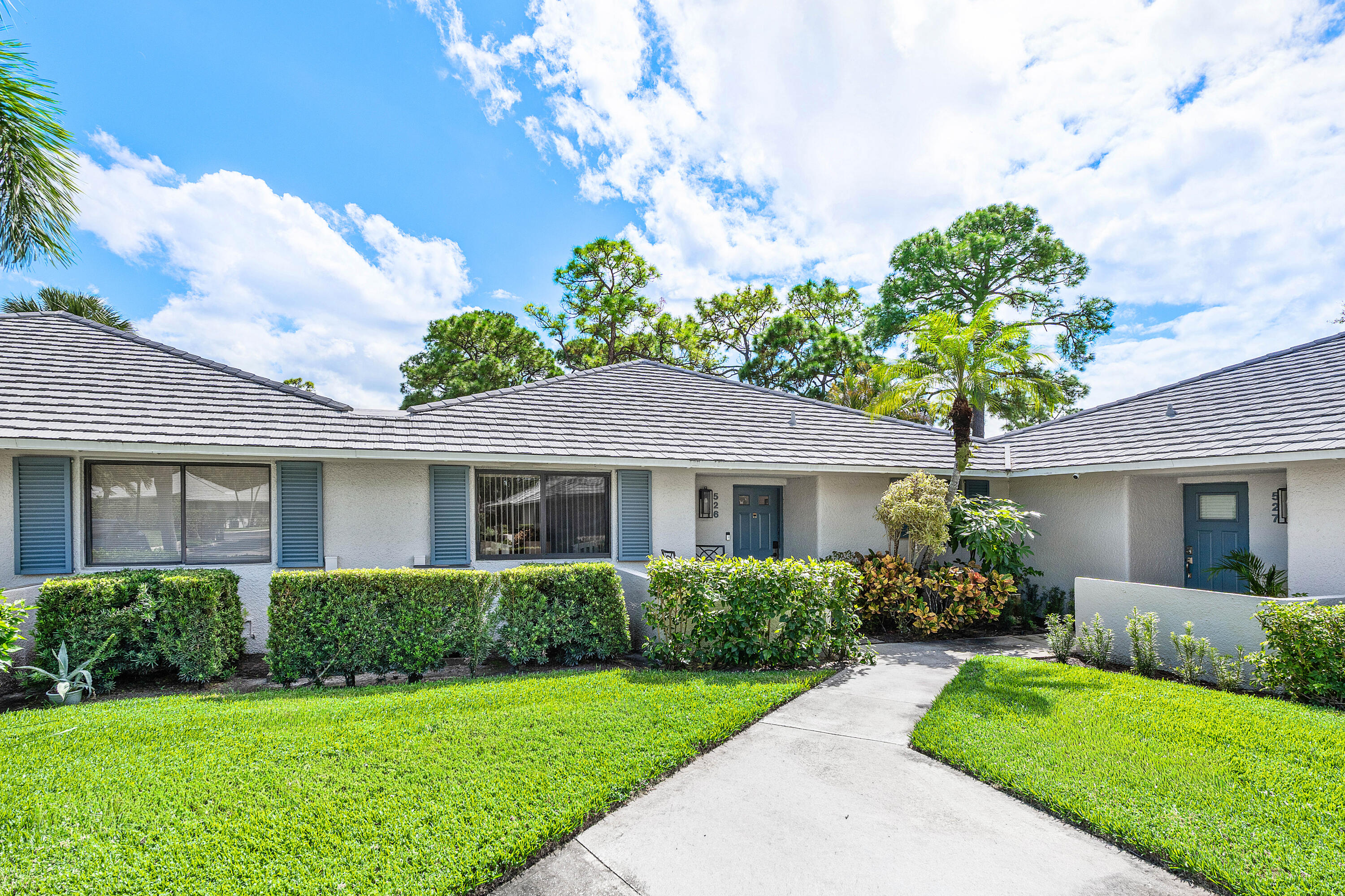 Single-story exterior featuring a concrete tile roof, neutral stucco finish, decorative shutters, and manicured landscaping