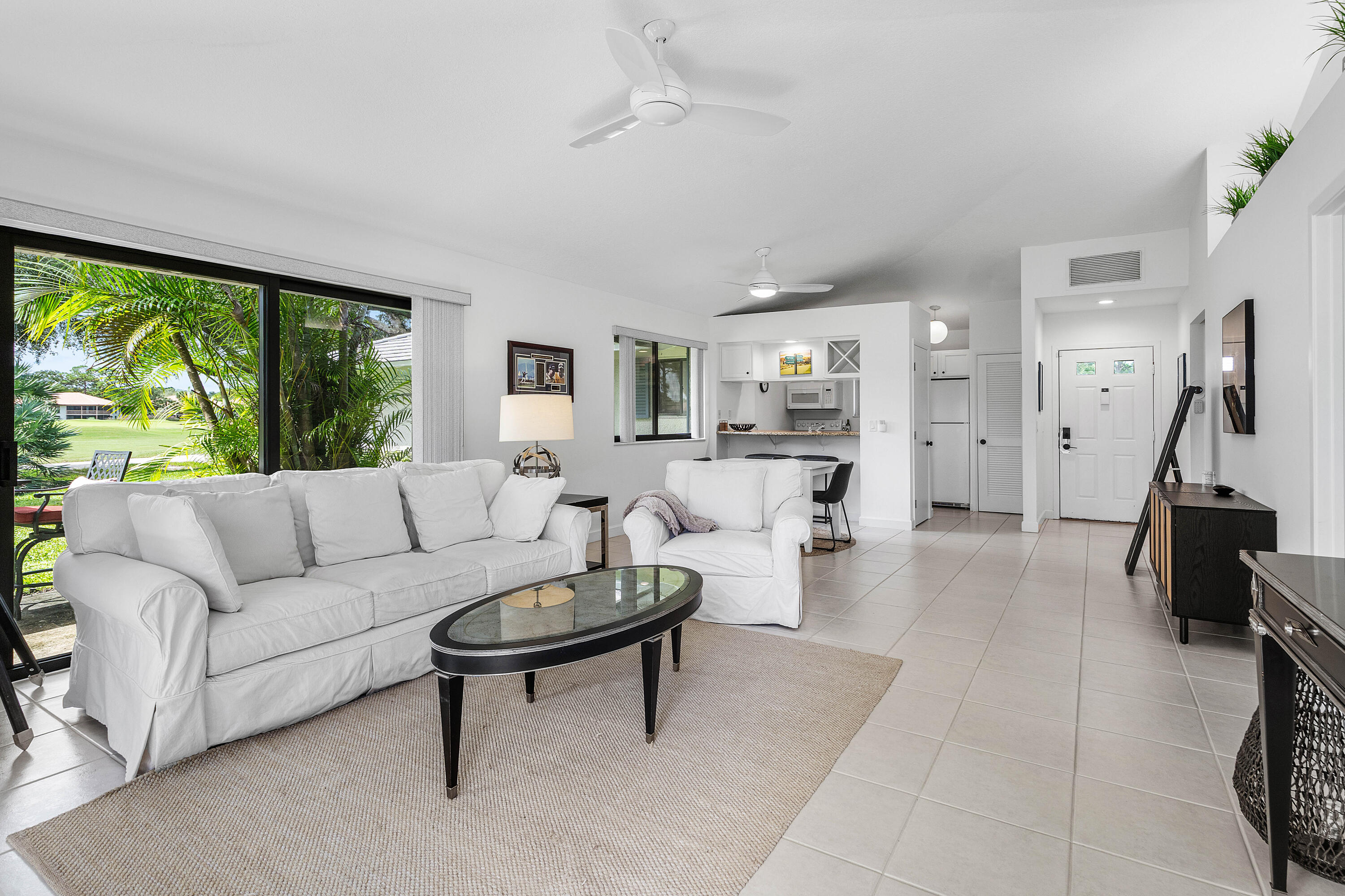 Open-concept living space featuring ceramic tile flooring, floor-to-ceiling sliding glass doors, built-in kitchen cabinetry, and overhead ceiling fans