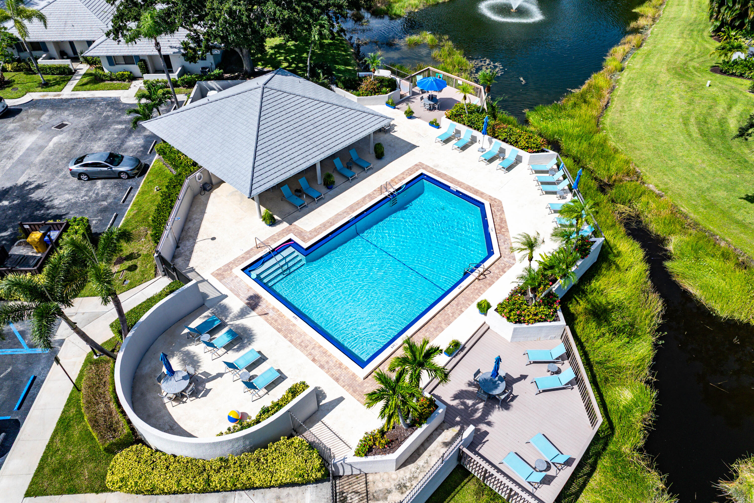 Community swimming pool featuring a geometric basin, surrounding paved deck, covered pavilion, and integrated landscaping