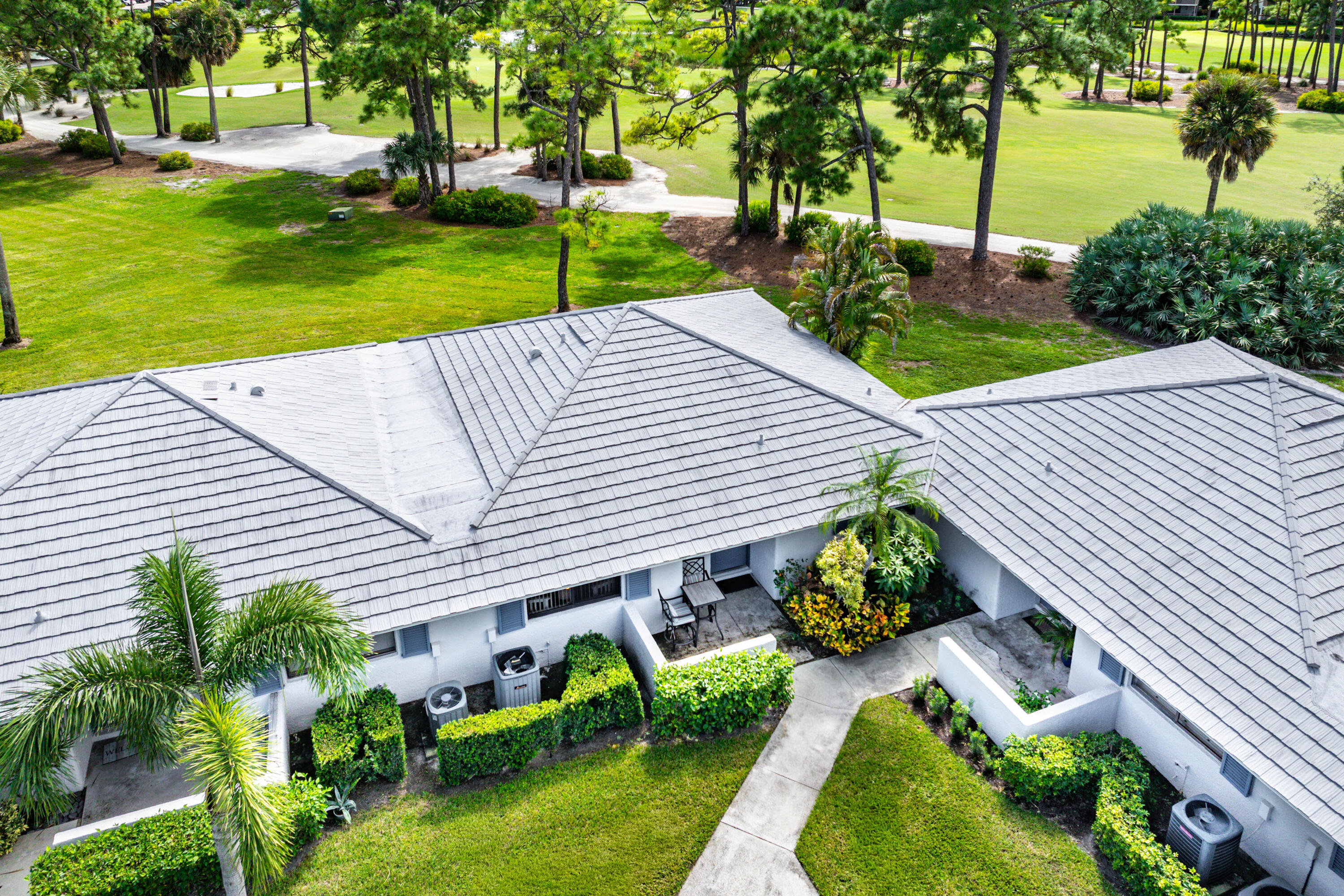 Multi-pitched concrete tile roof, manicured lawn, established landscaping, and paved walkway set against a backdrop of mature trees and open green space