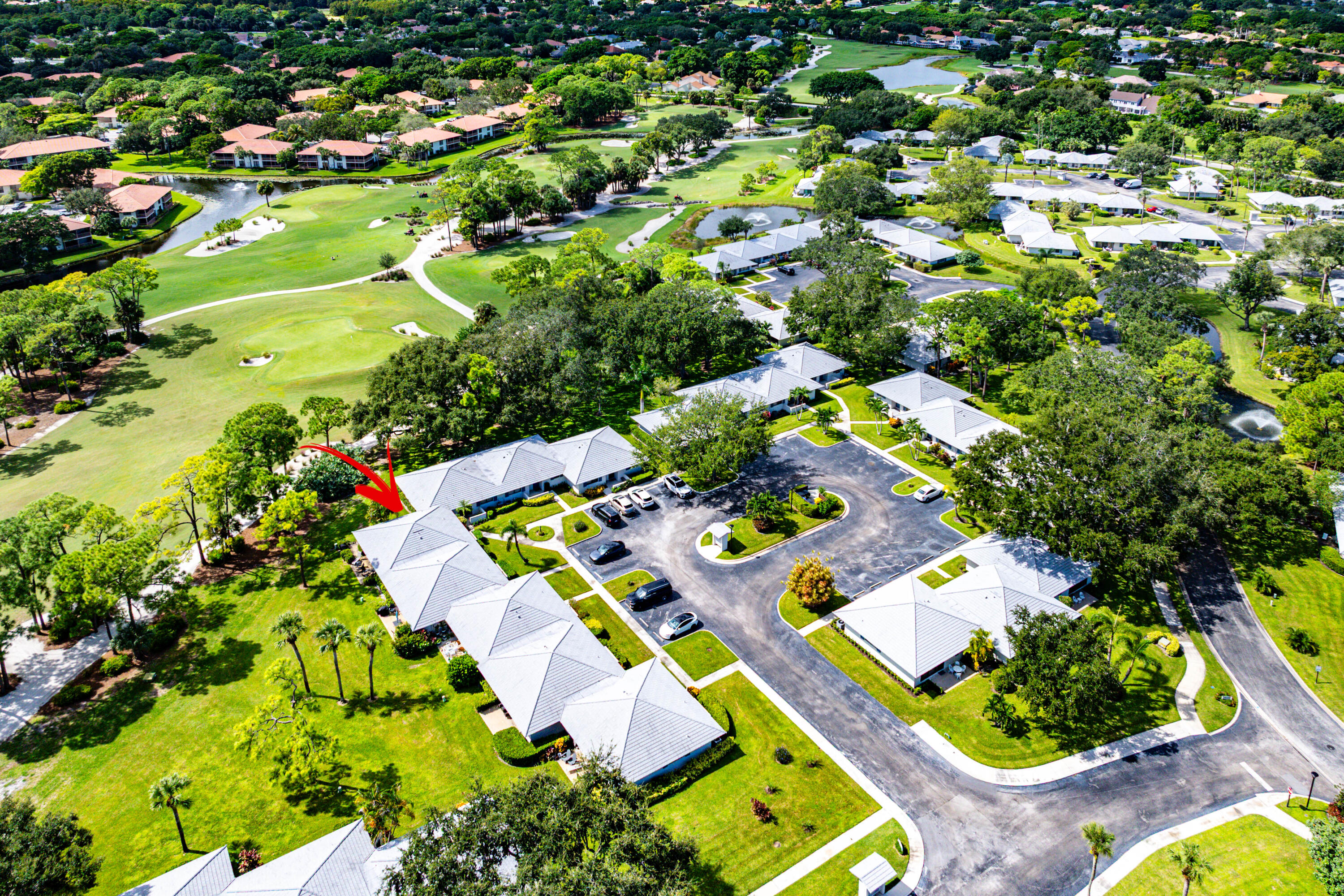 Aerial perspective featuring a single-story structure with a multi-gabled roof, positioned on a manicured lawn with mature trees and paved surface parking