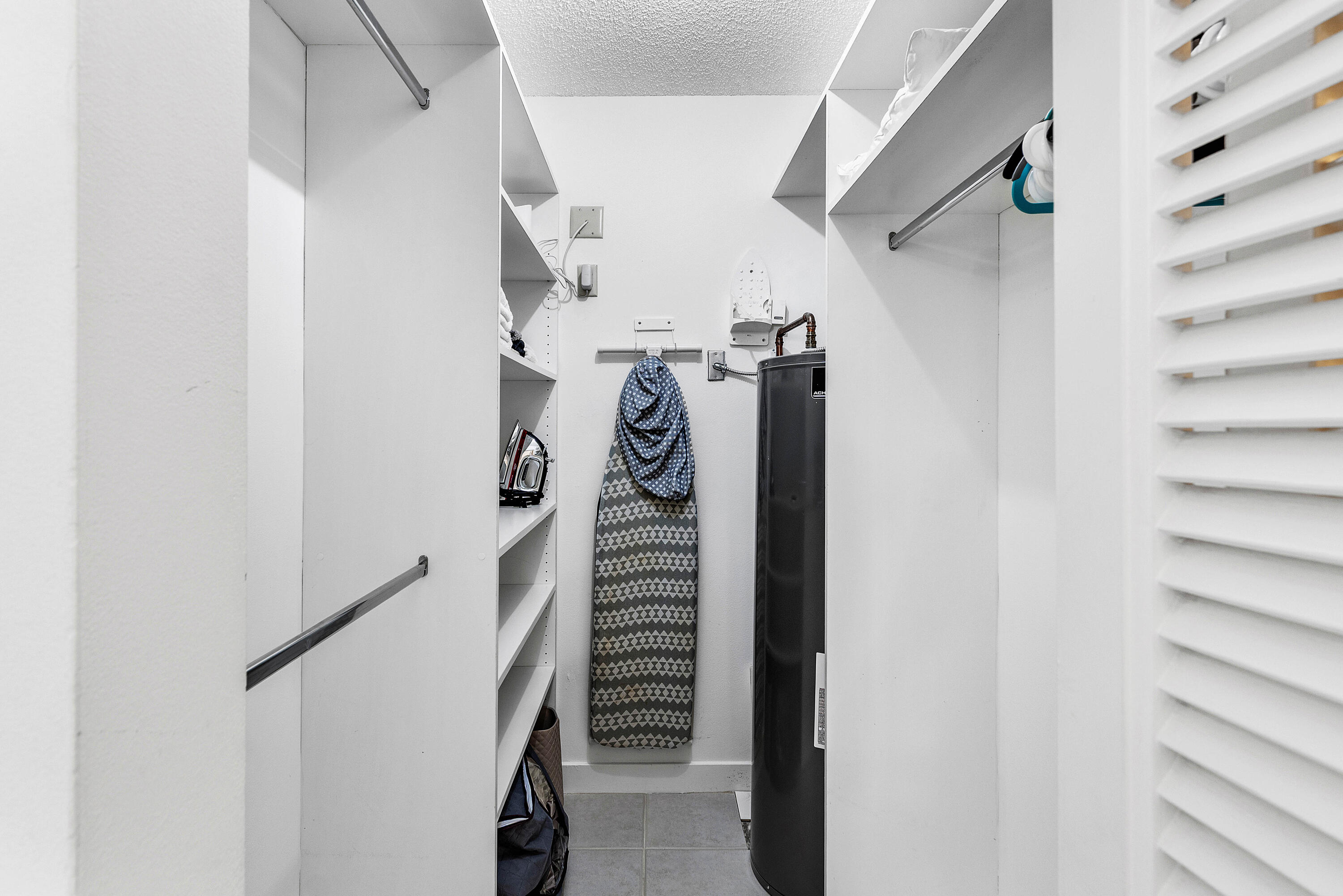 Walk-in closet featuring white built-in shelving, dual hanging rods, tile flooring, and louvered double doors