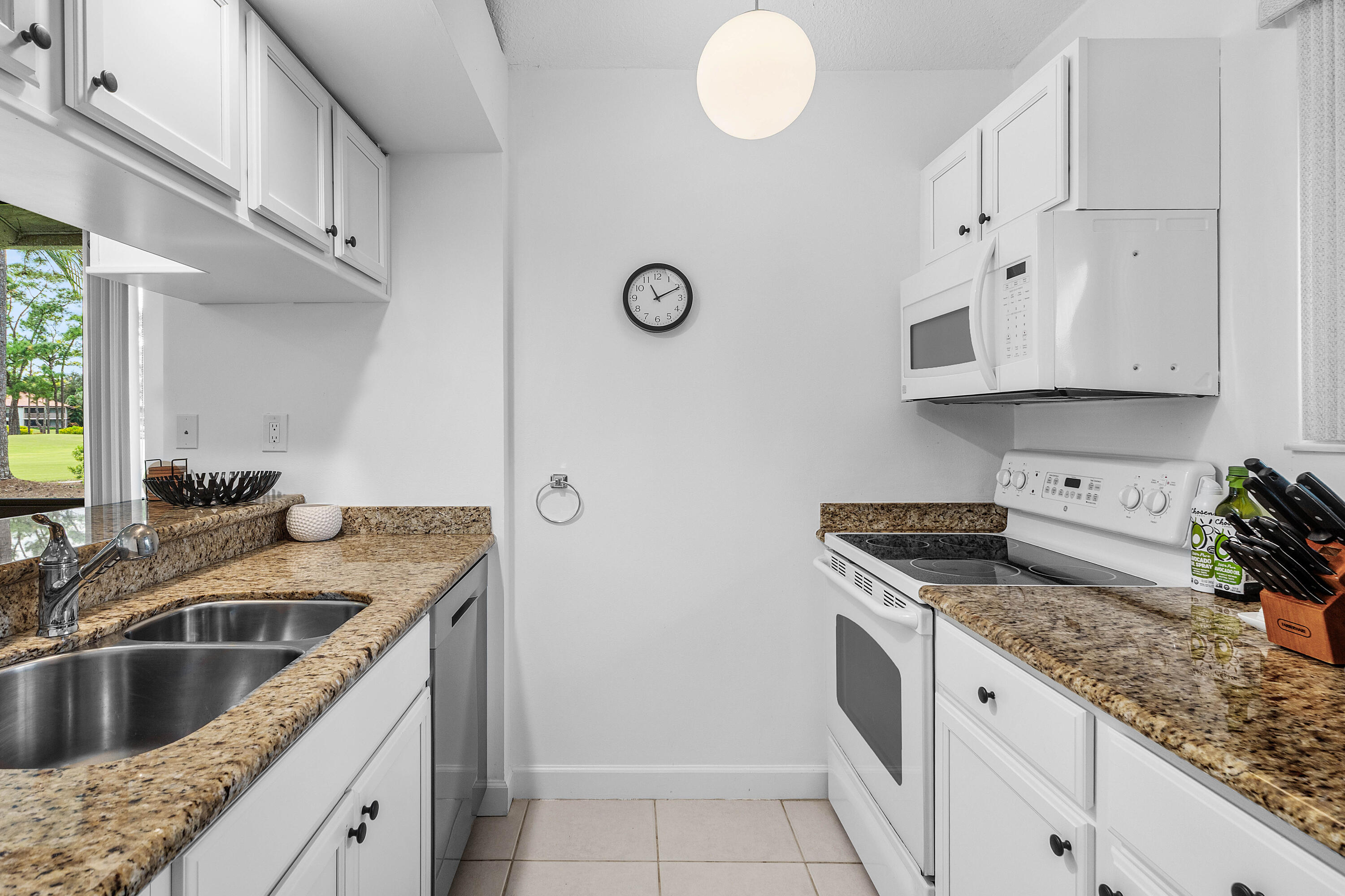 Kitchen featuring white cabinetry, stone-finish countertops, an integrated stainless steel double-basin sink, an over-the-range microwave, and ceramic tile flooring