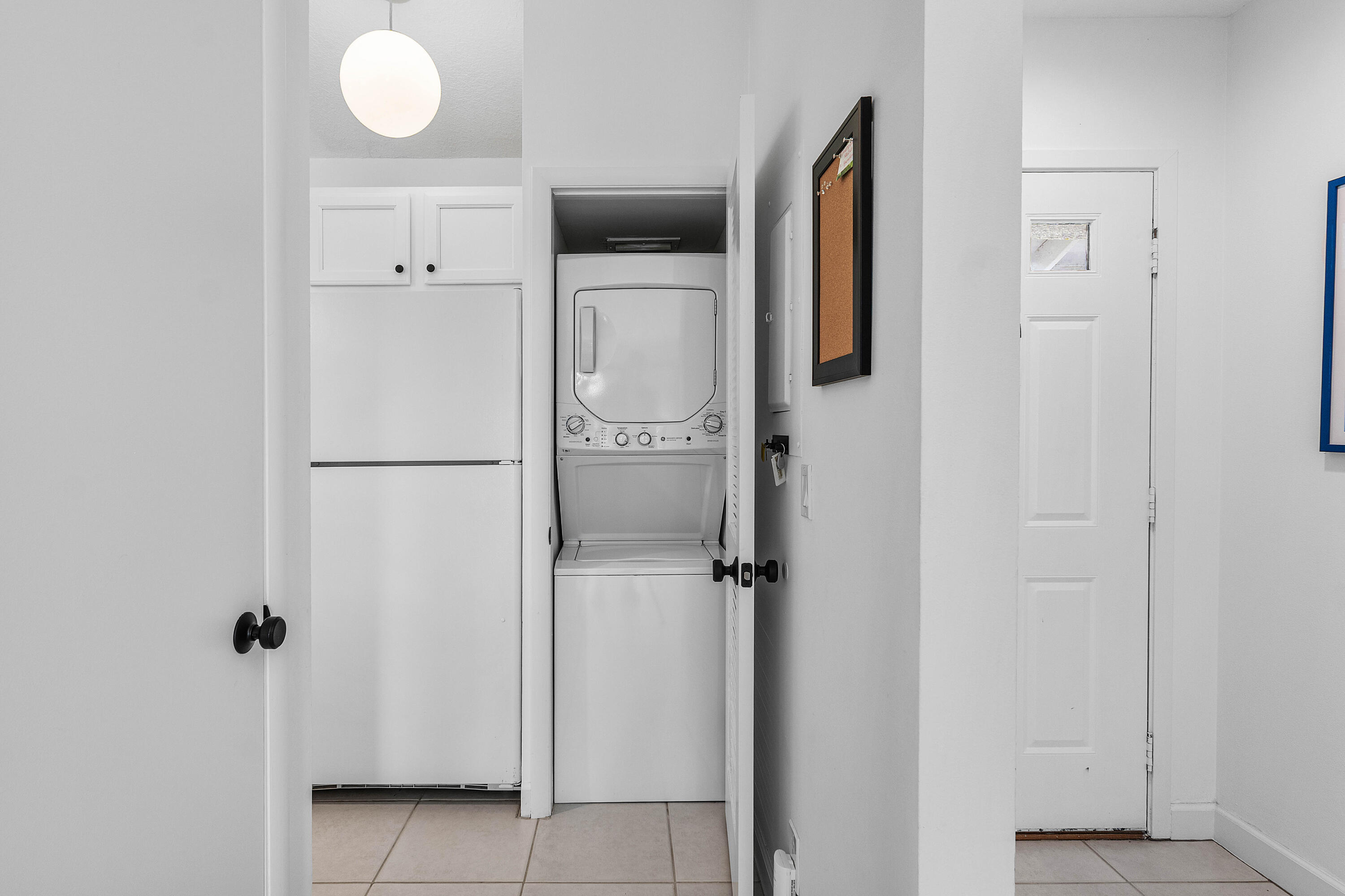Utility area featuring stacked laundry appliances, white cabinetry, ceramic tile flooring, and a globe pendant light fixture