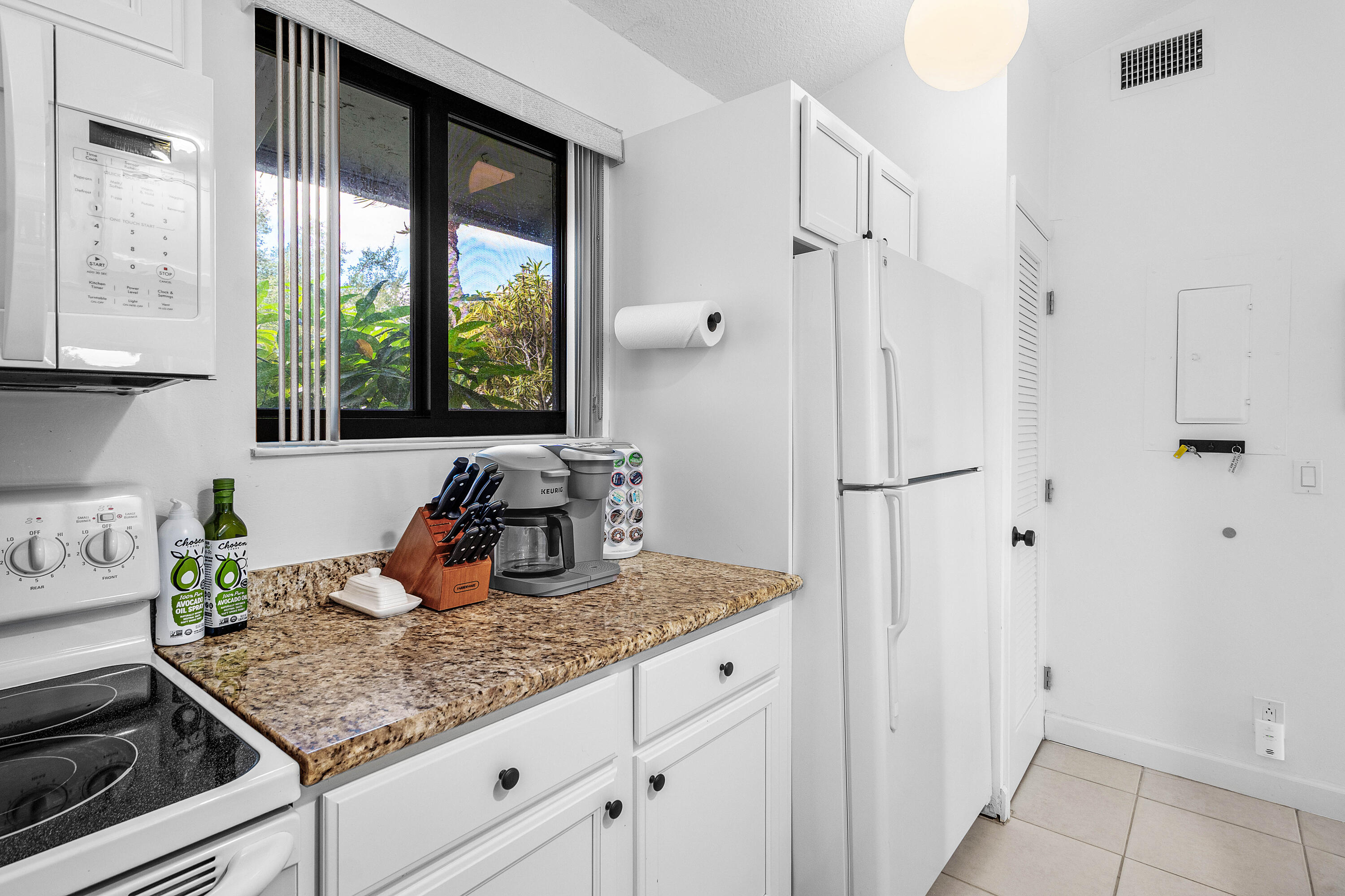 Kitchen featuring white shaker-style cabinetry, stone-finish countertops, tile flooring, and built-in appliances