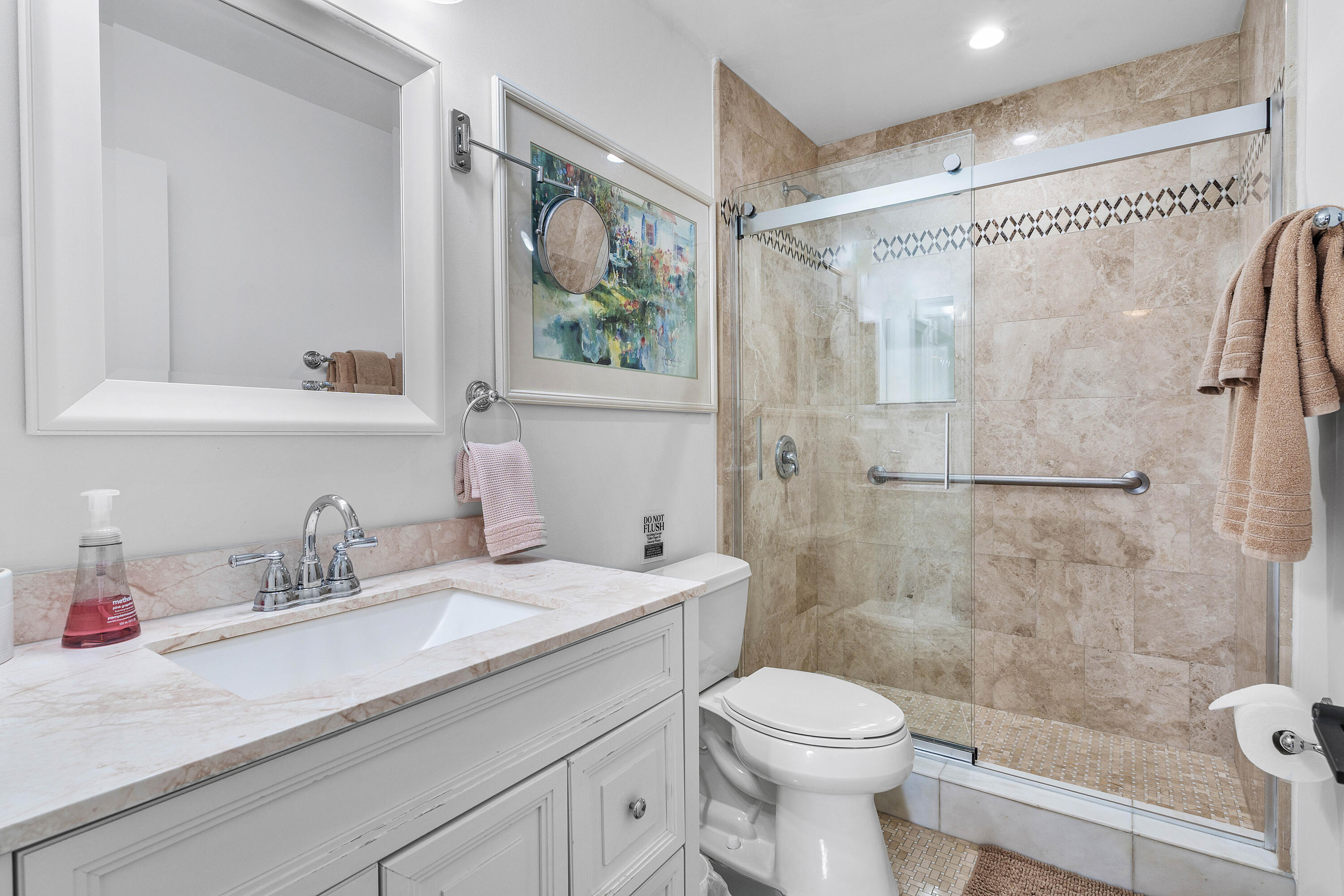 Bathroom featuring a white vanity with stone countertop, undermount sink, framed mirror, and a walk-in shower with stone tile surround and sliding glass doors