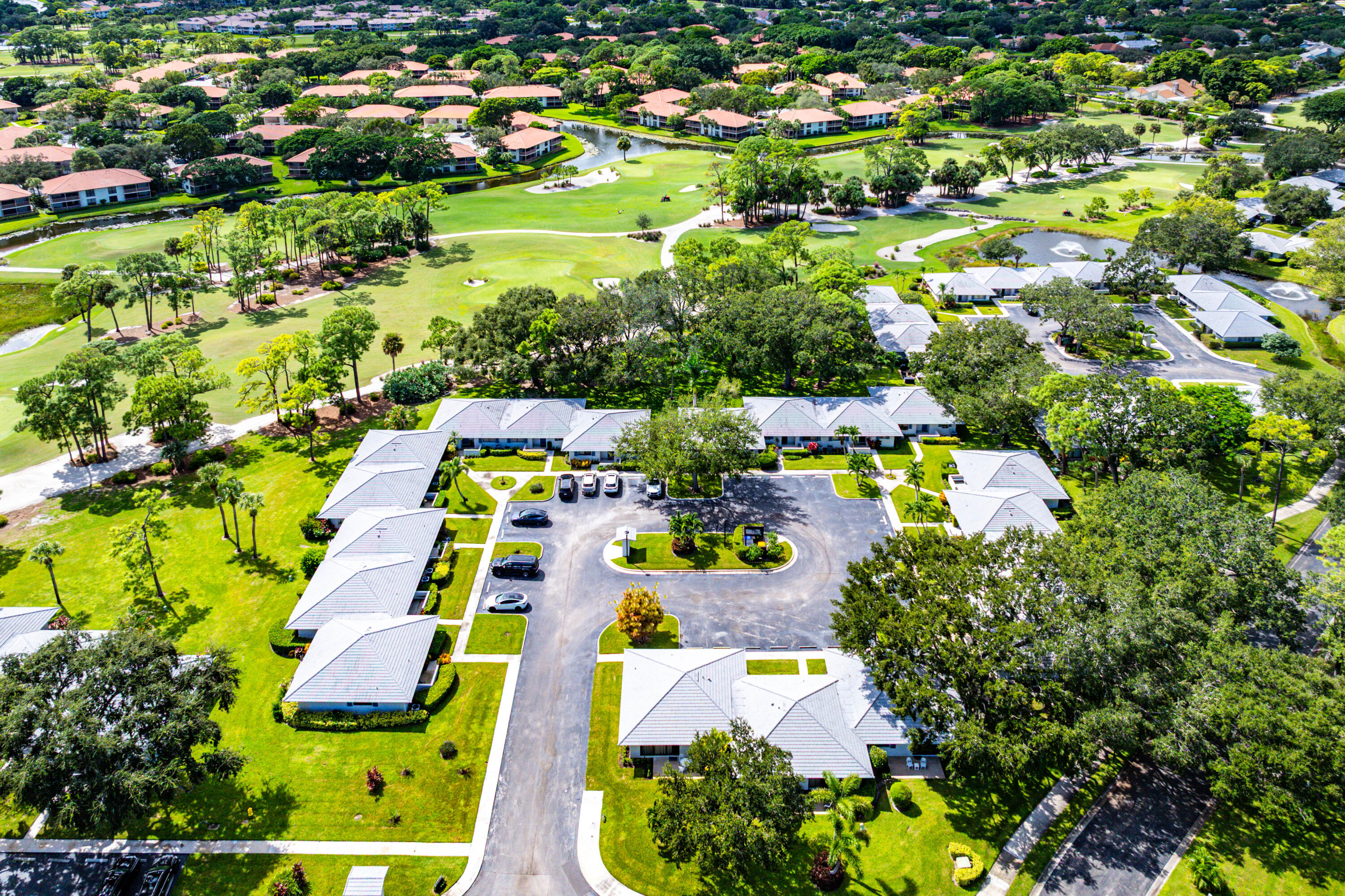 Aerial perspective of a multi-unit residential complex featuring paved driveways, a central circular cul-de-sac, tile roofing, and expansive grounds with mature trees
